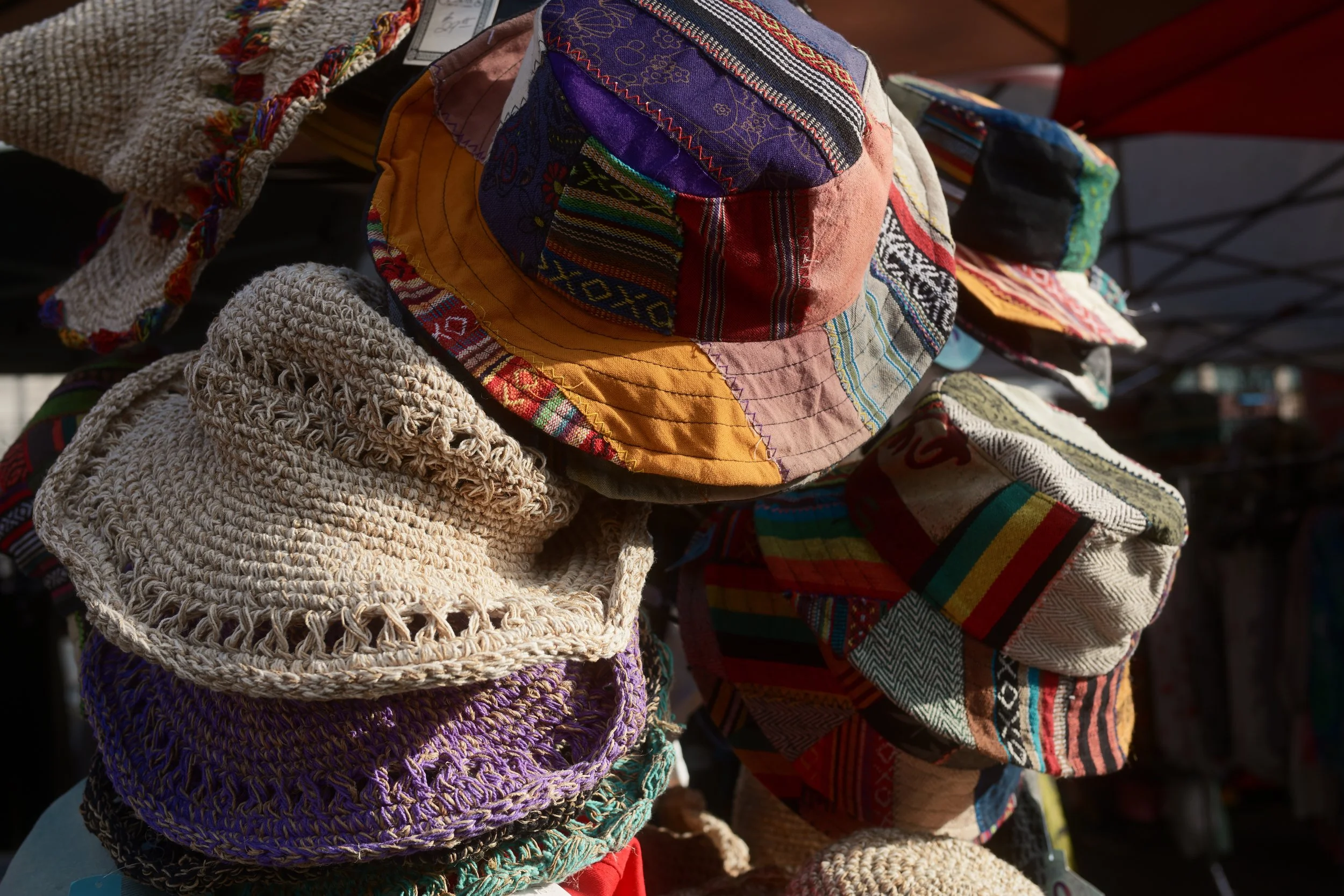Display of colorful, handcrafted fabric hats at an outdoor market stand.