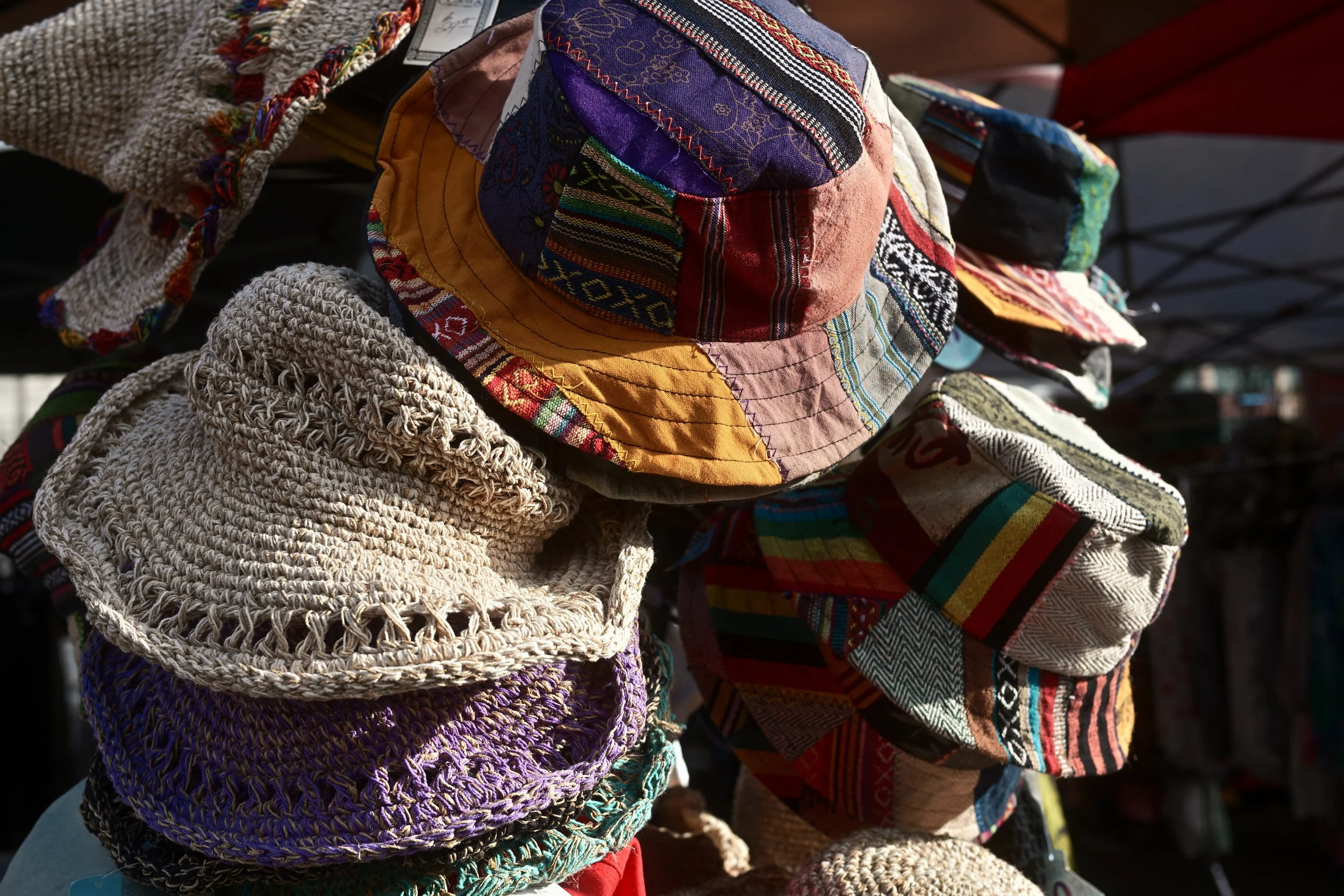 Colorful patchwork hats and woven hats displayed on a rack at an outdoor market.