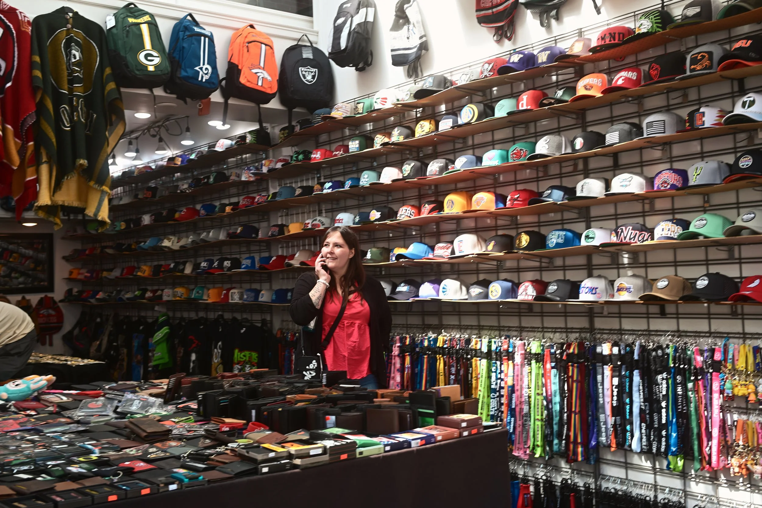 A woman shopping in a store with walls filled with hats and backpacks, and a table displaying wallets and accessories.