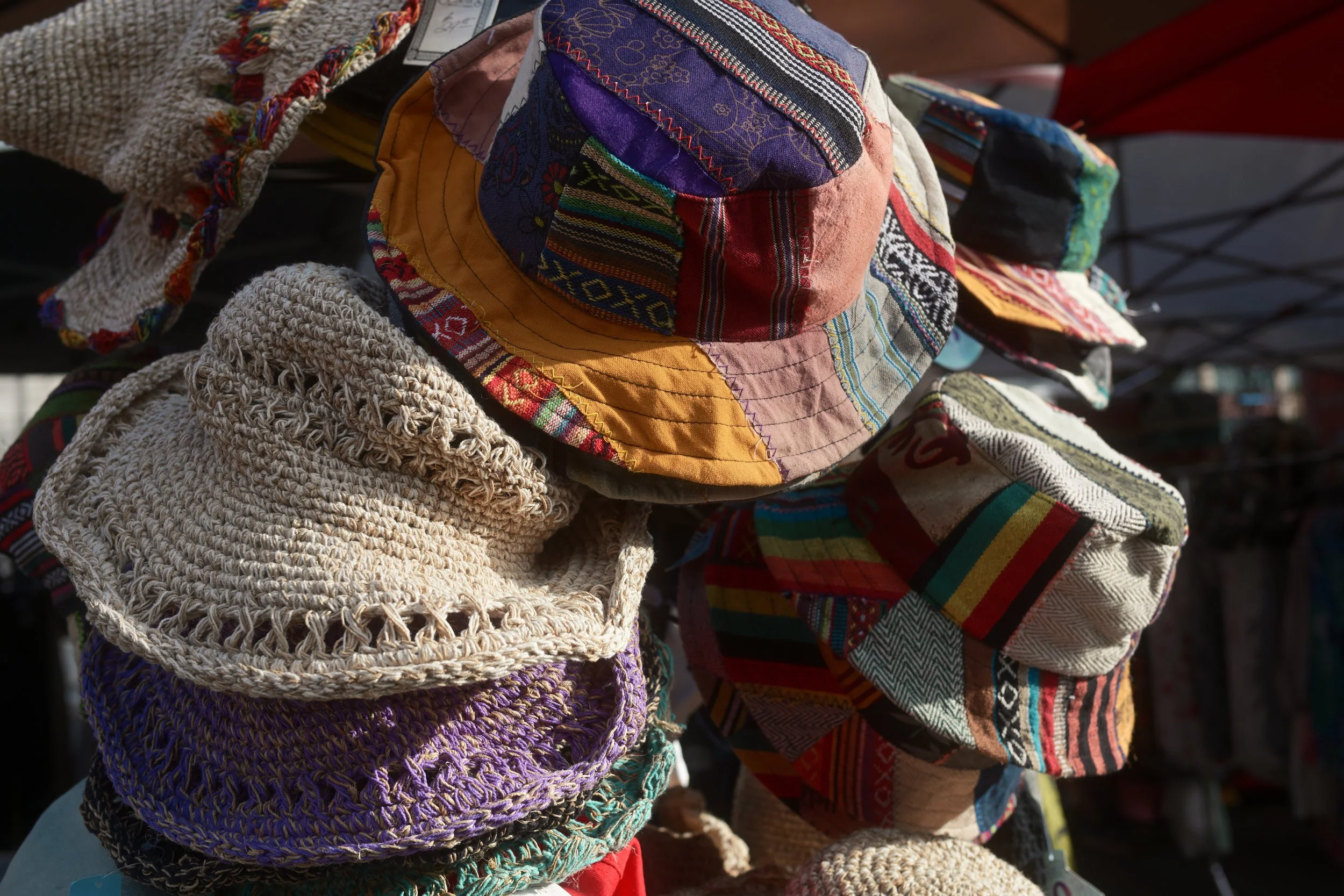 Colorful handmade hats and woven accessories displayed at an outdoor market.