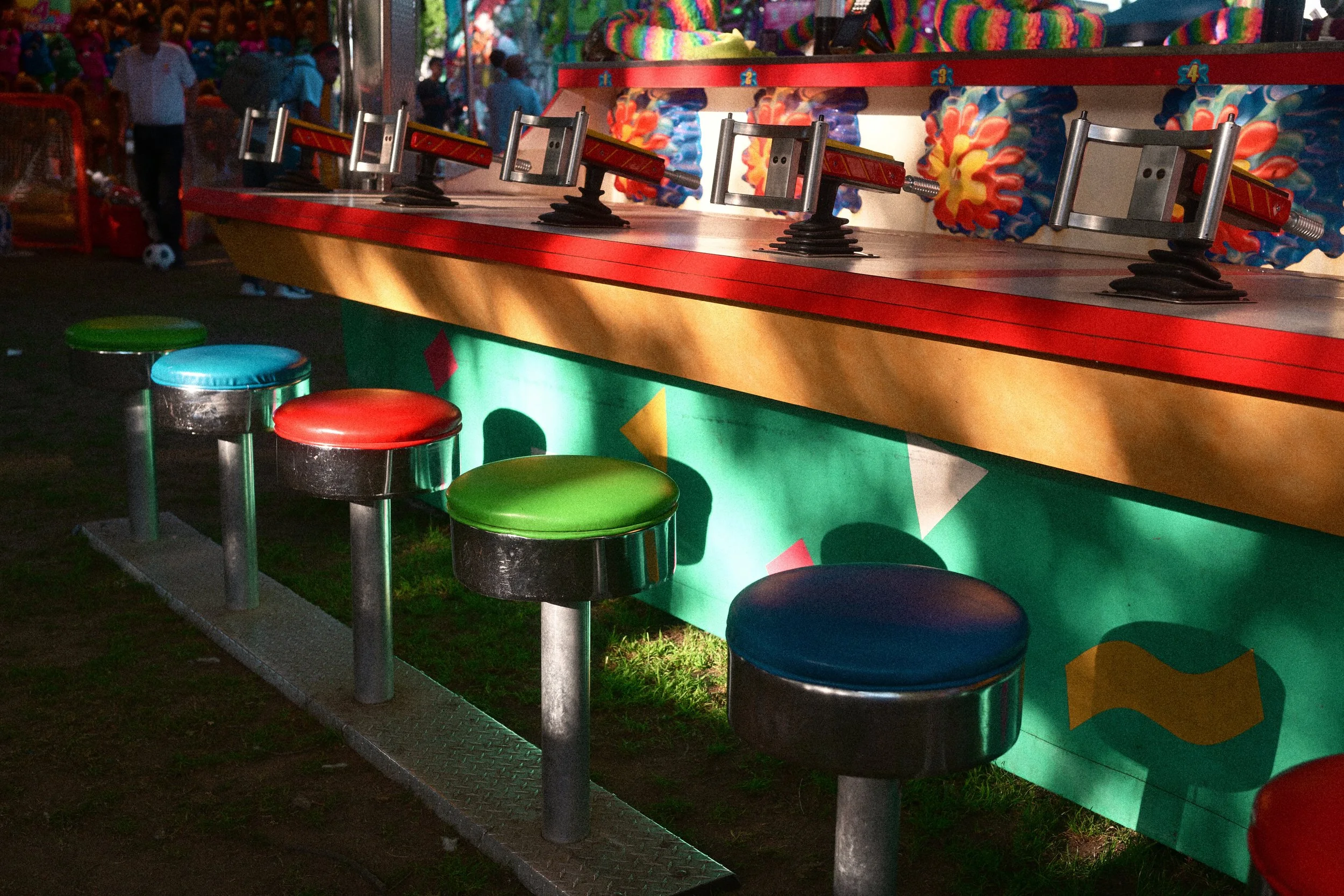 Colorful carnival shooting gallery with mounted toy rifles, numbered targets, and bright stools