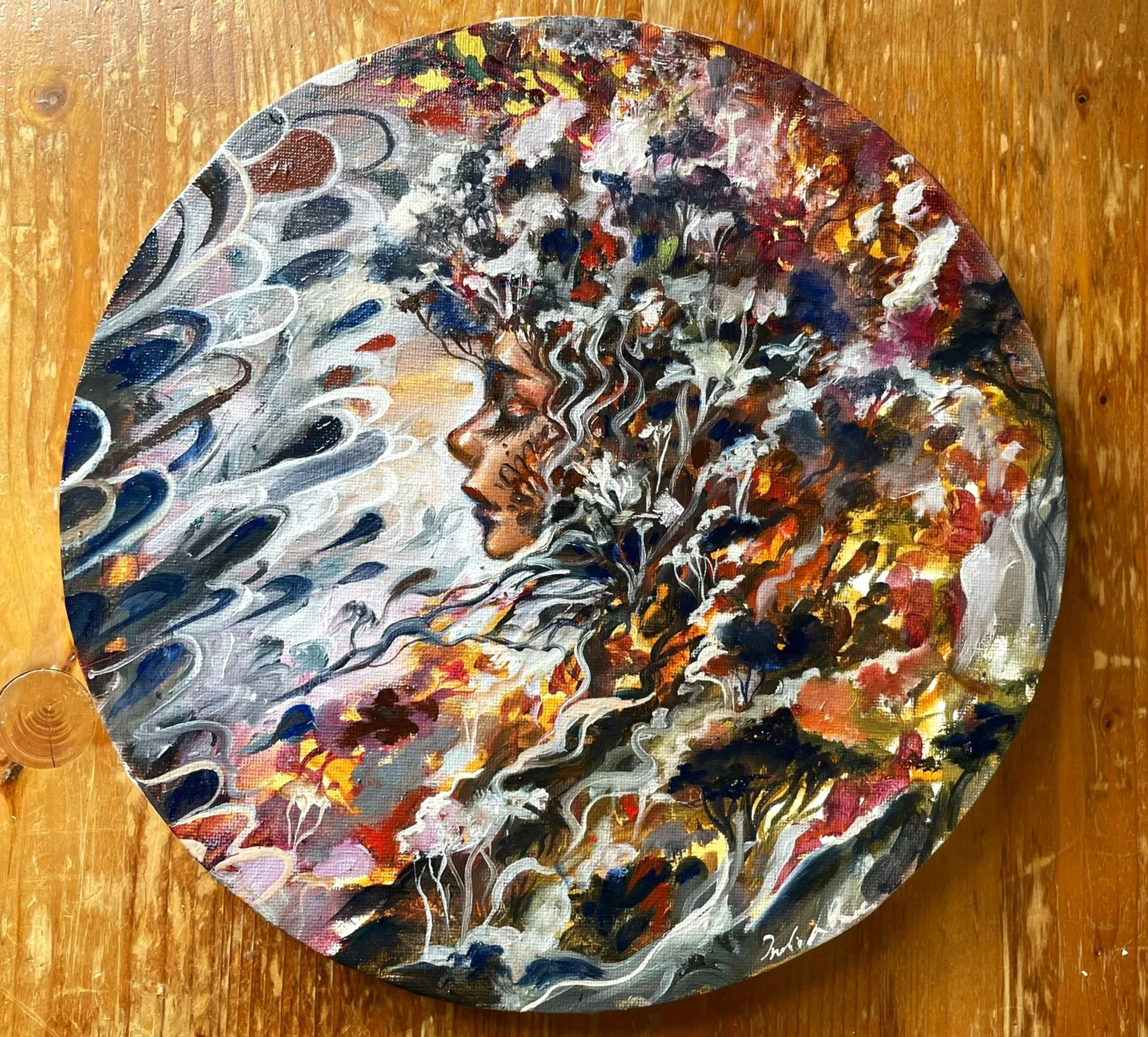 A round painting depicting a woman’s profile with flowing hair blending into an abstract floral design, featuring a mix of vibrant colors including white, black, red, orange, and yellow.