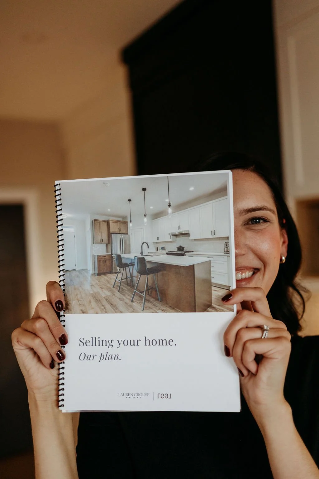 Person holding a real estate brochure with "Selling your home. Our plan." and a kitchen image on the cover.