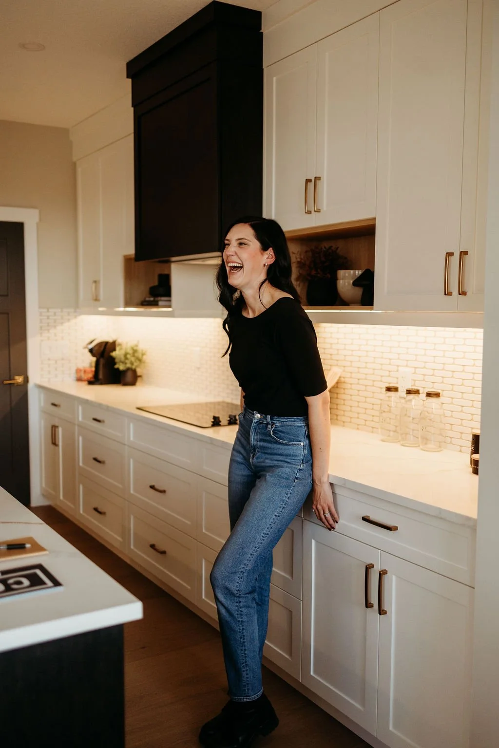 Person laughing in a modern kitchen with white cabinets and dark accents.
