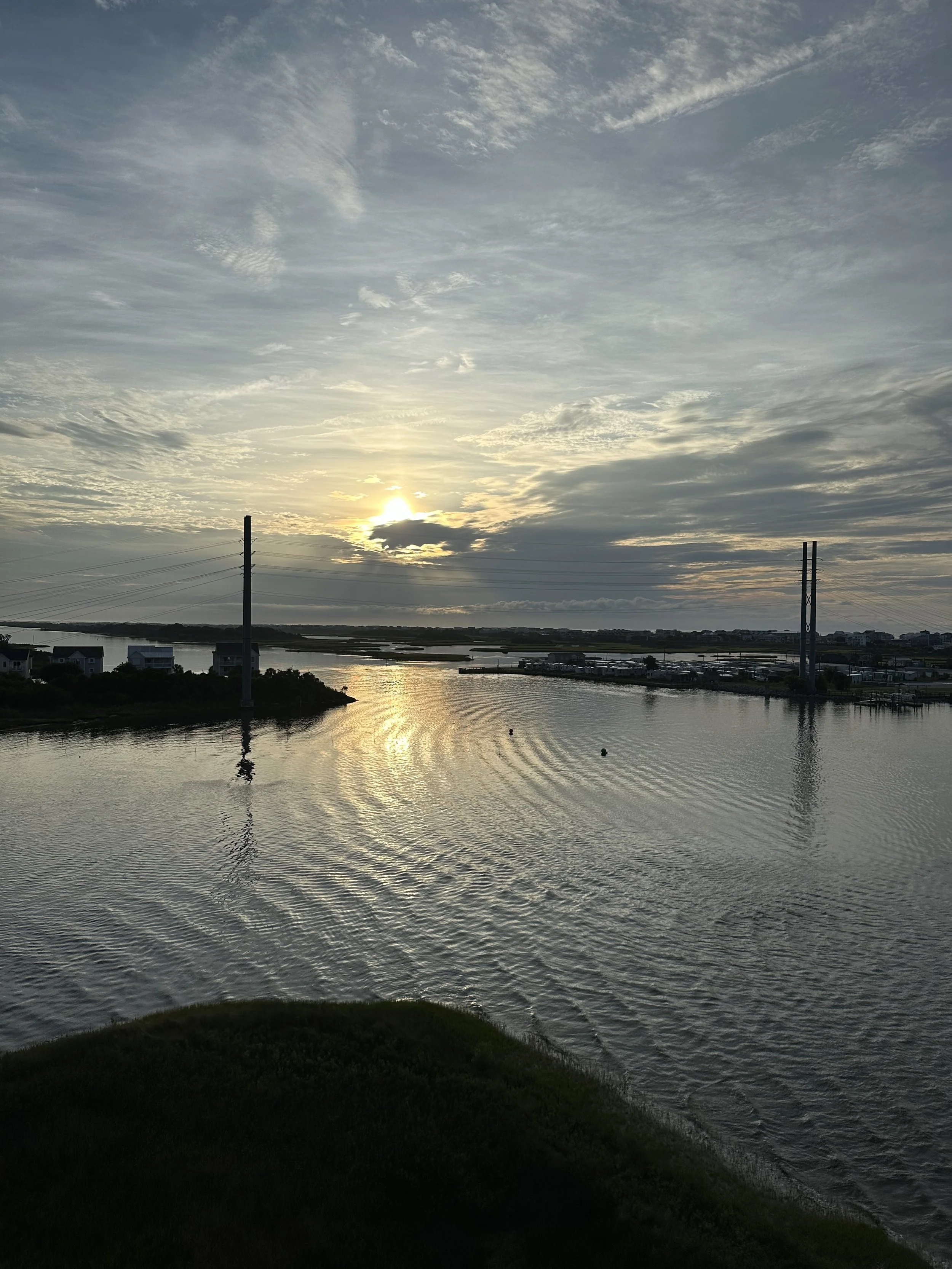A sunset over a body of water with ripples and a partly cloudy sky.