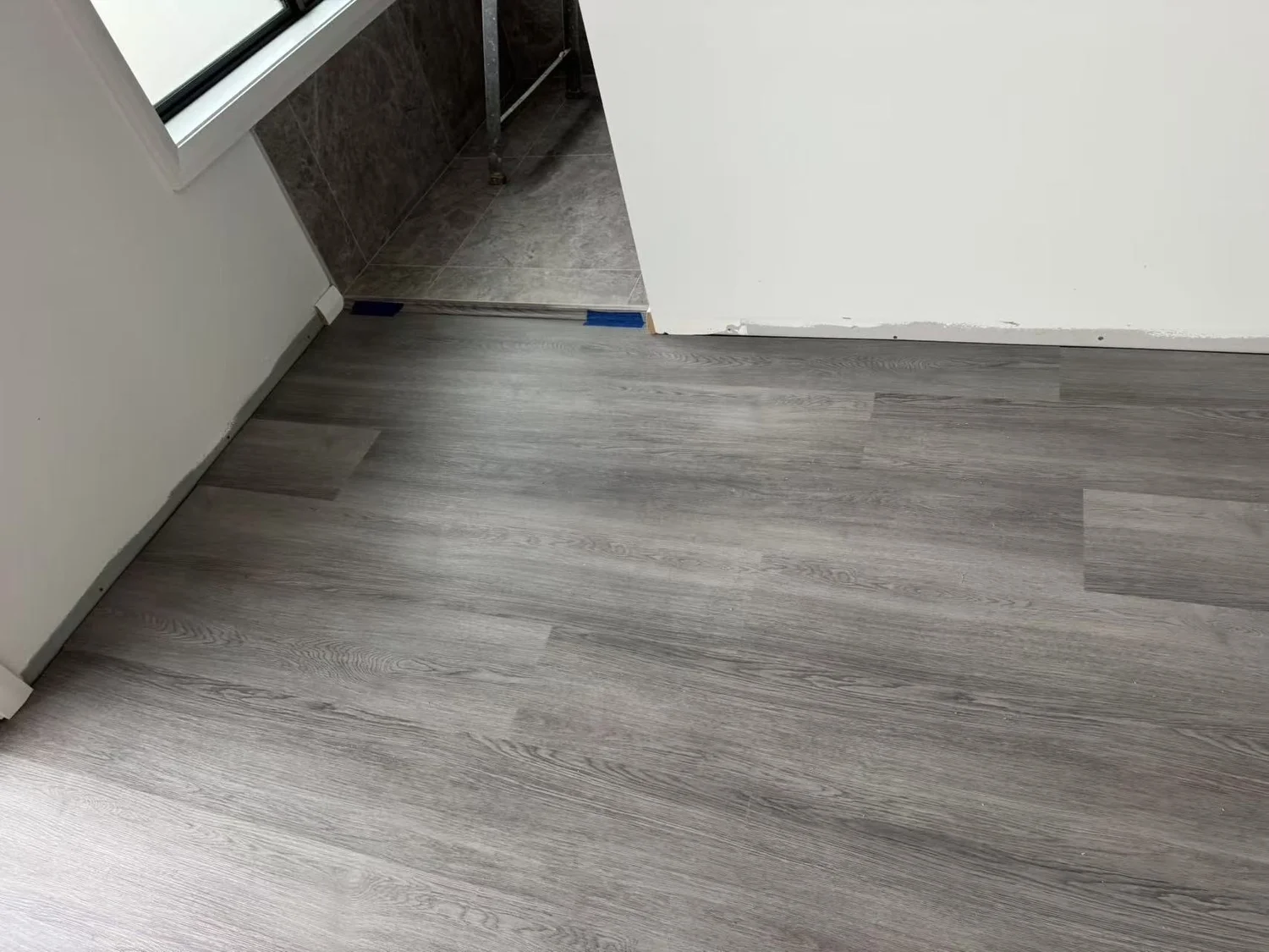 Room with light gray wood laminate flooring and a doorway leading to a tiled area with a metal ladder.