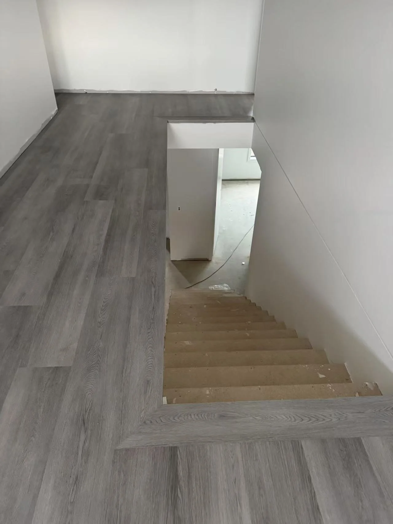 View of a staircase with wooden steps, balcony with grey wood flooring, and white walls in a house under construction or renovation.