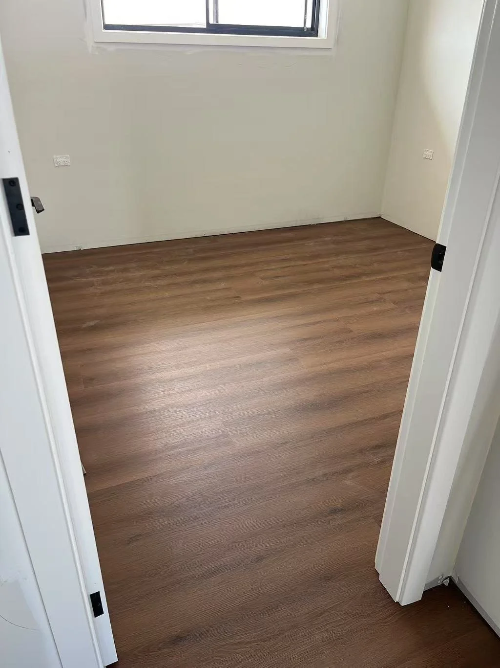 Empty room with wooden flooring, white walls, a window, and electrical outlets.