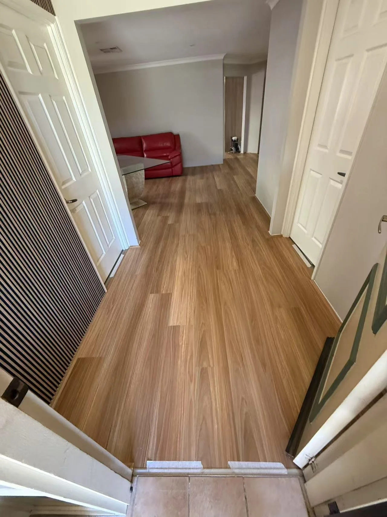 Entryway with wooden flooring, white walls, and a curved staircase in the background. A red leather couch is partially visible in the adjacent room.