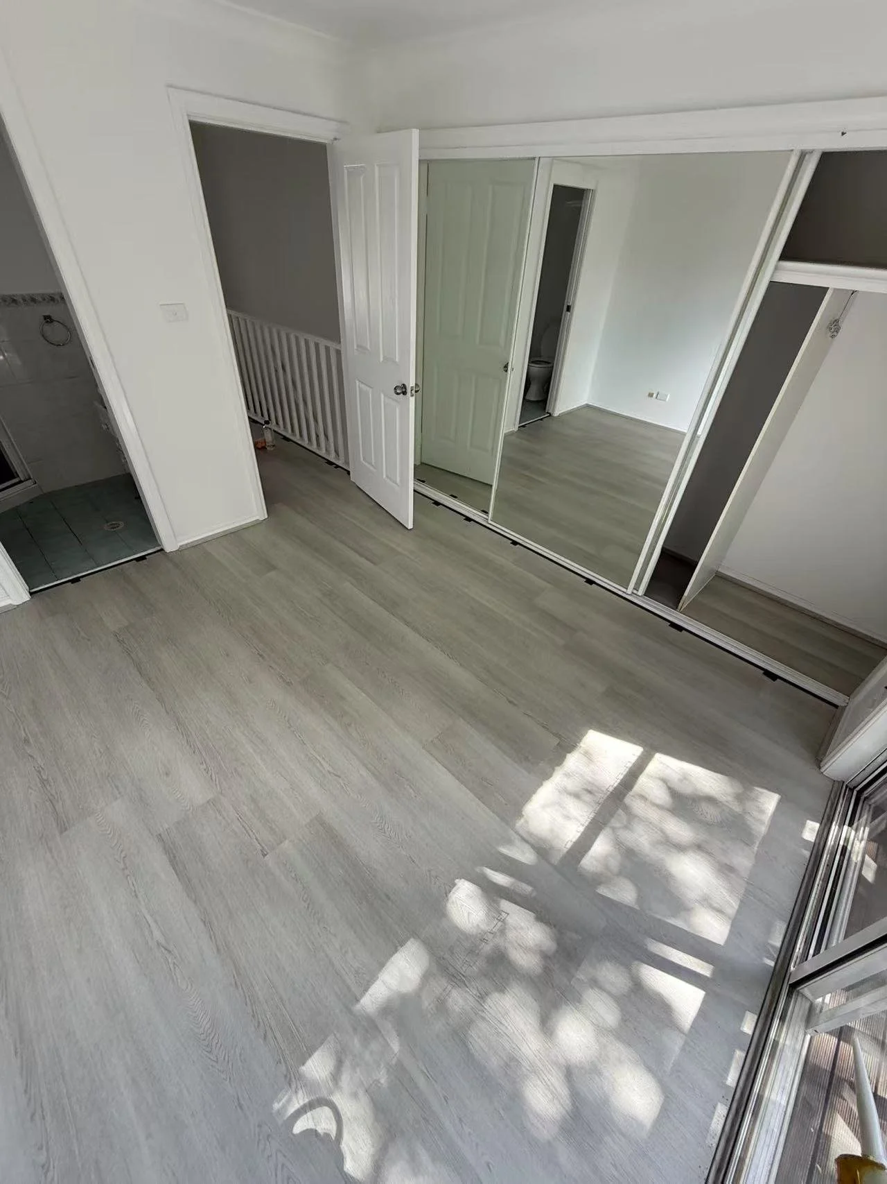 Empty room with light wood flooring, mirror sliding closet doors, view of bathroom, and partially visible bathroom shower in the corner.