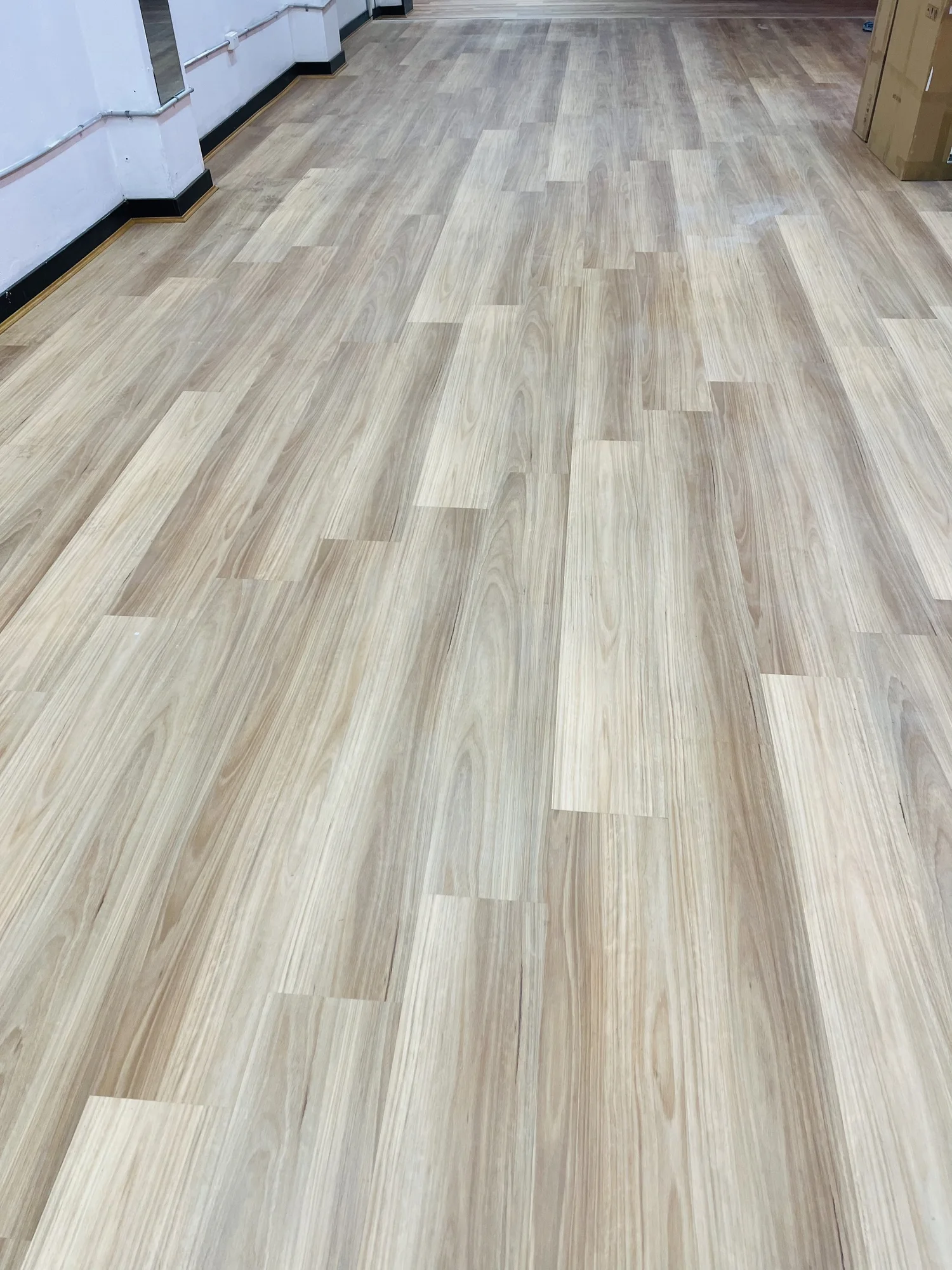 Smooth, light-colored wood laminate flooring in a room with white walls and black baseboards, with some brown cardboard boxes visible in the corner.