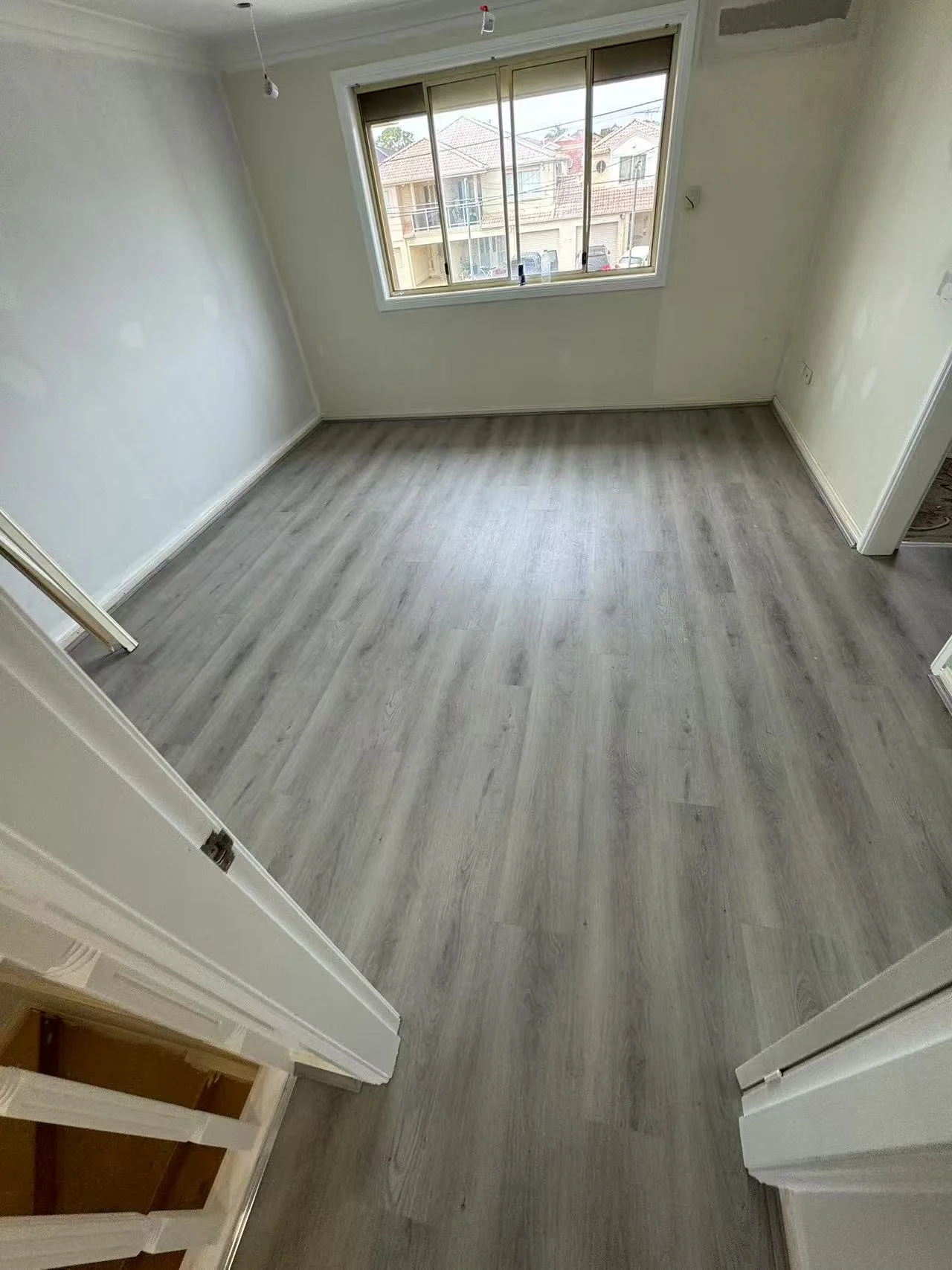 Empty room with light gray flooring, white walls, and a large window showing exterior houses.