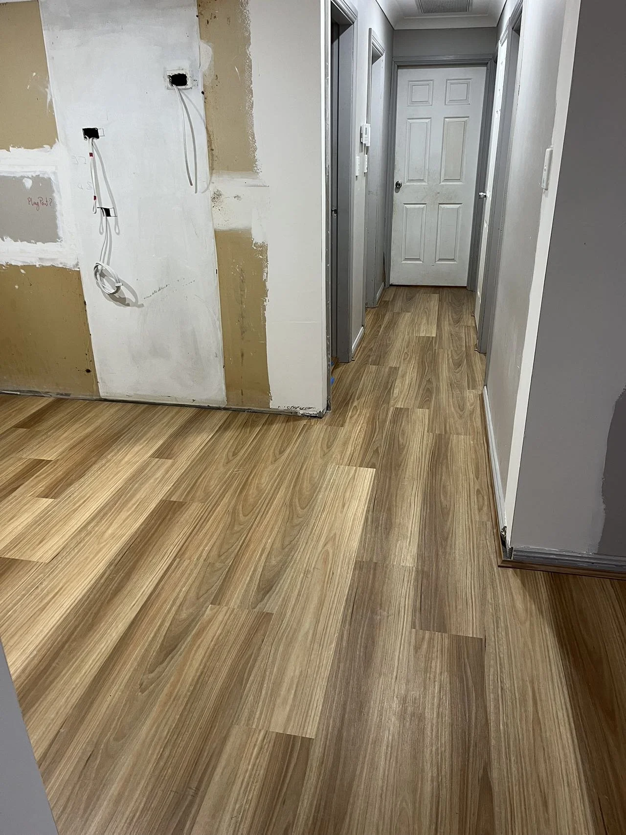 Interior of a house with new wood-look flooring, unfinished walls, and wiring for electrical outlets.