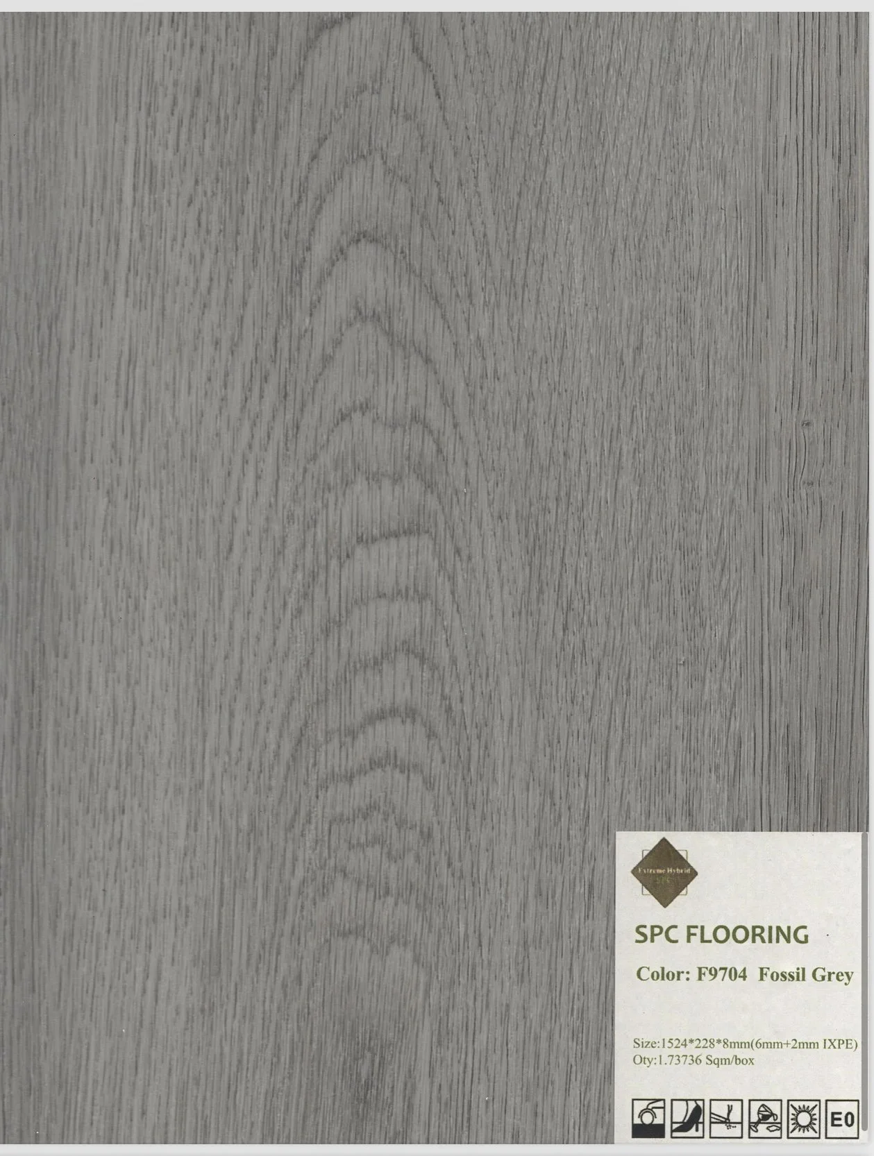 Gray SPC flooring sample with wood grain pattern and a label in the lower right corner indicating the color as Fossil Grey.