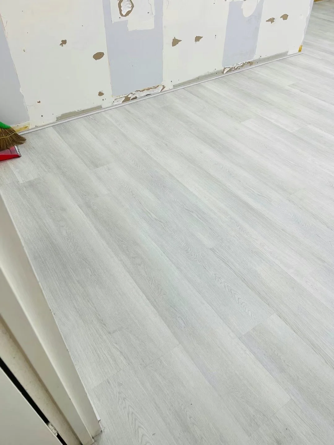 Room with partially removed drywall and new light-colored laminate flooring.