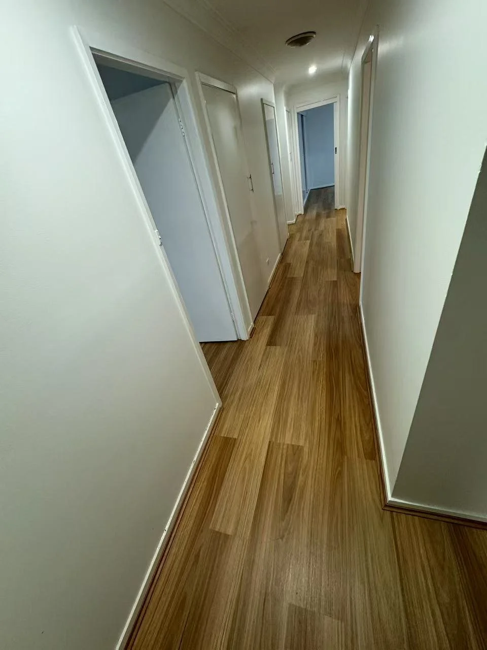 Empty hallway with white walls and wood flooring, multiple closed doors along the corridor.