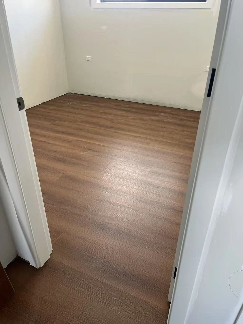 Empty room with light-colored walls, wood-look flooring, and a window.