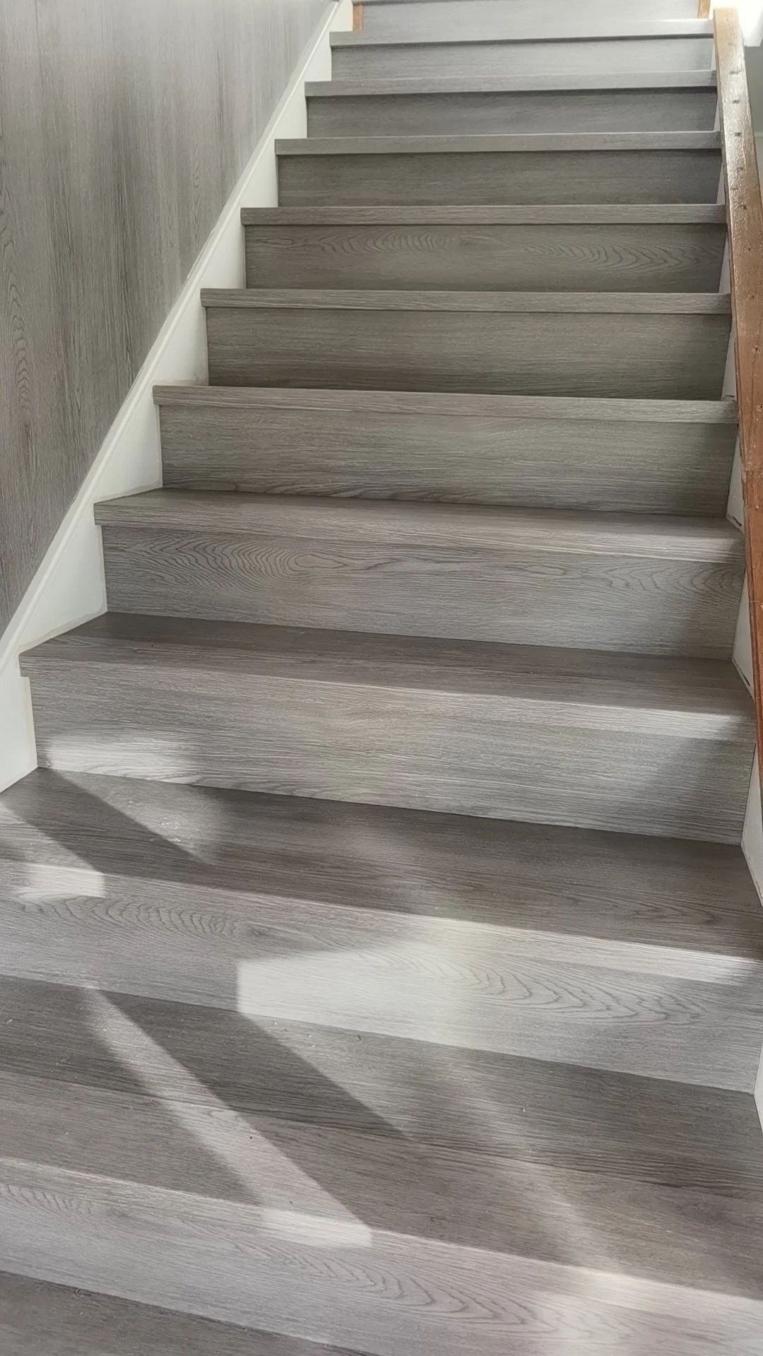 Grey wooden staircase with white trim and grey wall on the left side, sunlight casting shadows on the steps.
