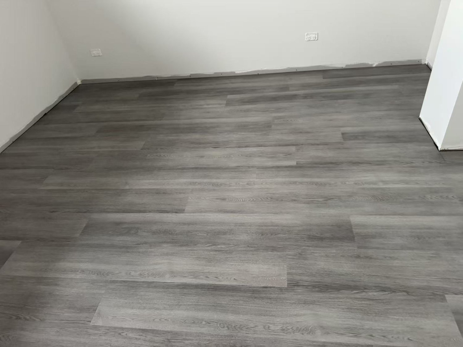 Room with newly installed gray wooden flooring, white walls, and electrical outlets.
