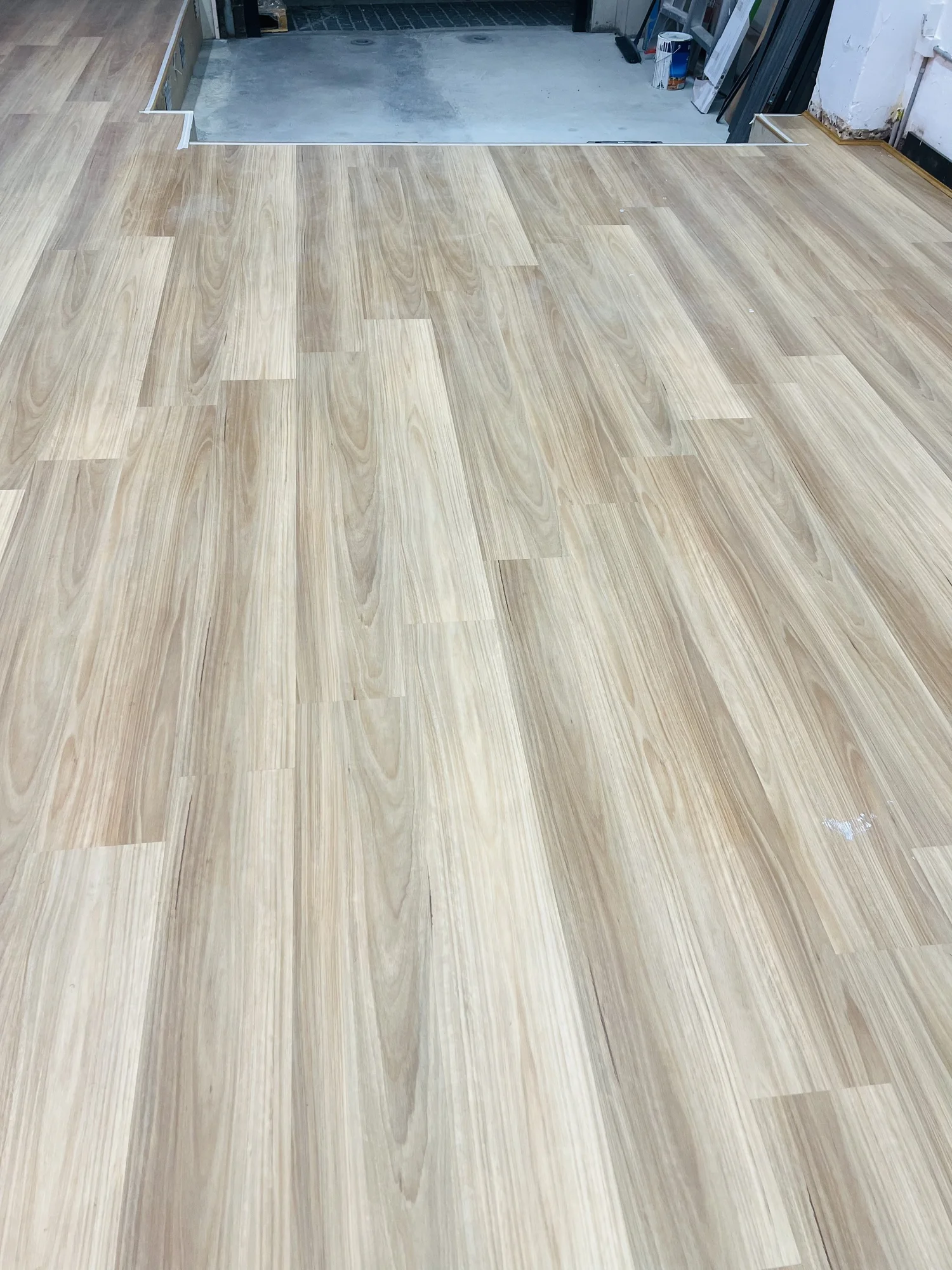 New light-colored wooden flooring being installed in a room, with some tools and building materials visible in the background.