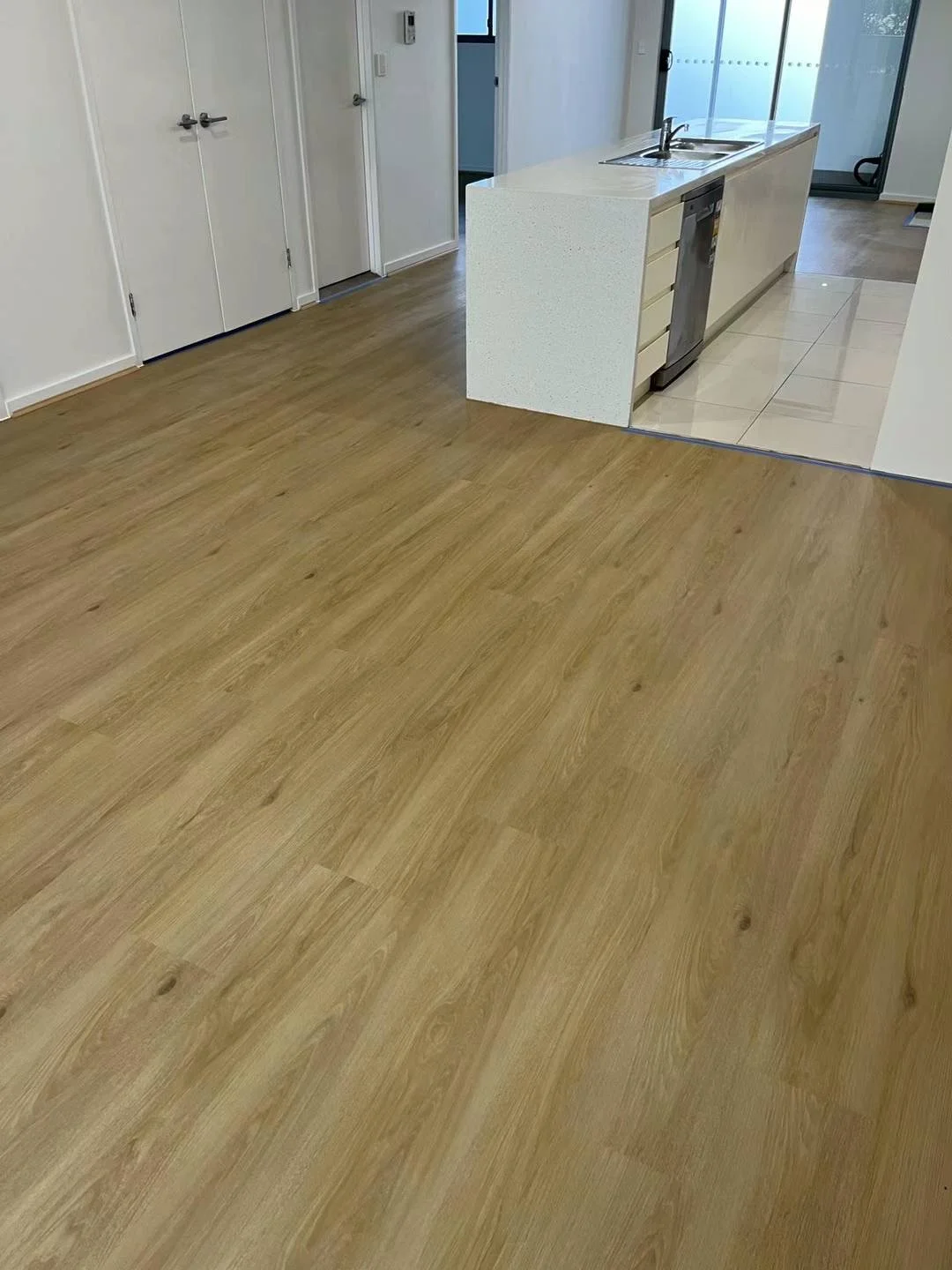 Room with wood flooring transitioning to tiled kitchen area with white cabinets and a kitchen sink.