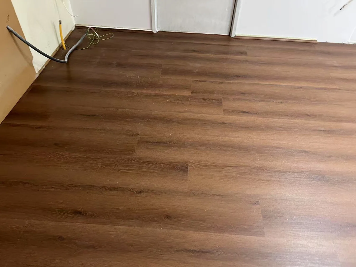 Finished hardwood floor installation in a room with some electrical cables and an unfinished wall.