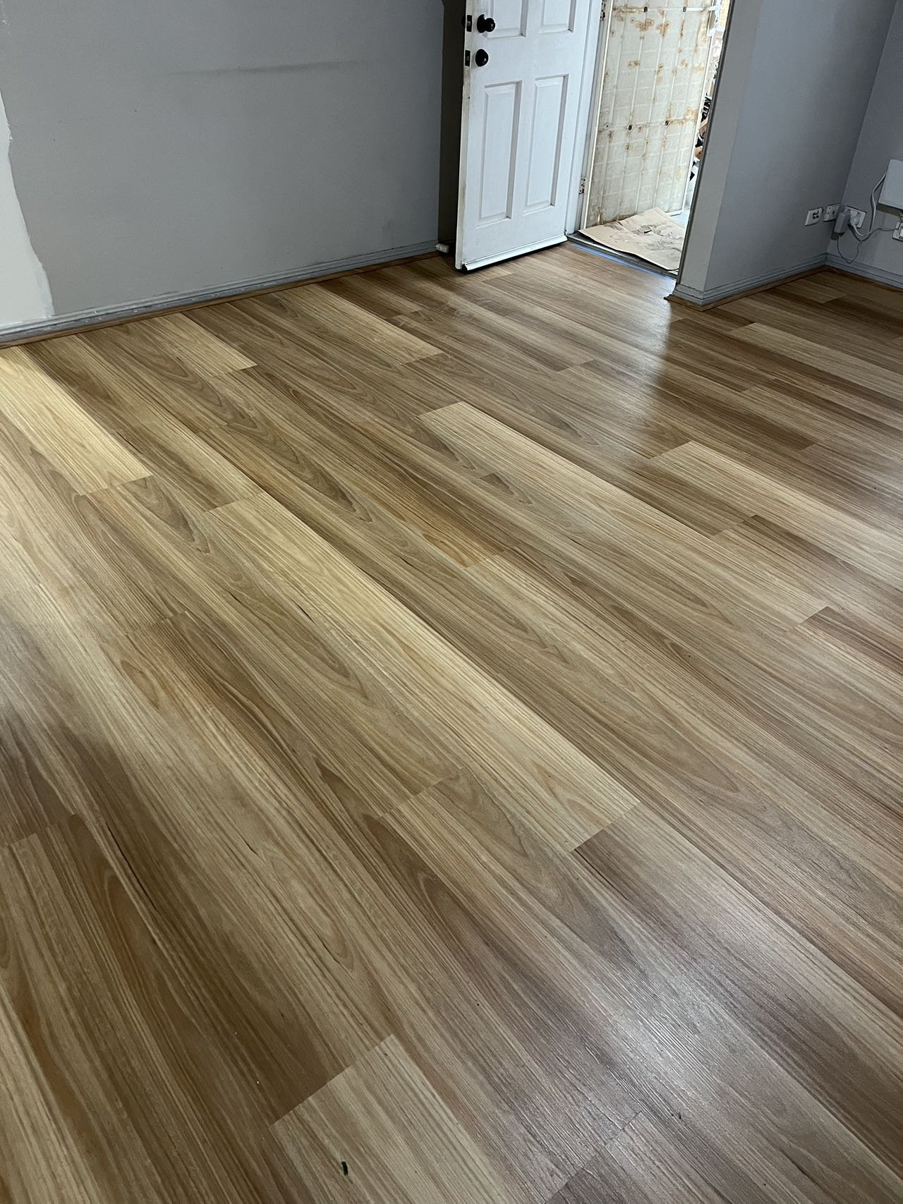 Newly installed hardwood floor in a room with an open door leading outside.