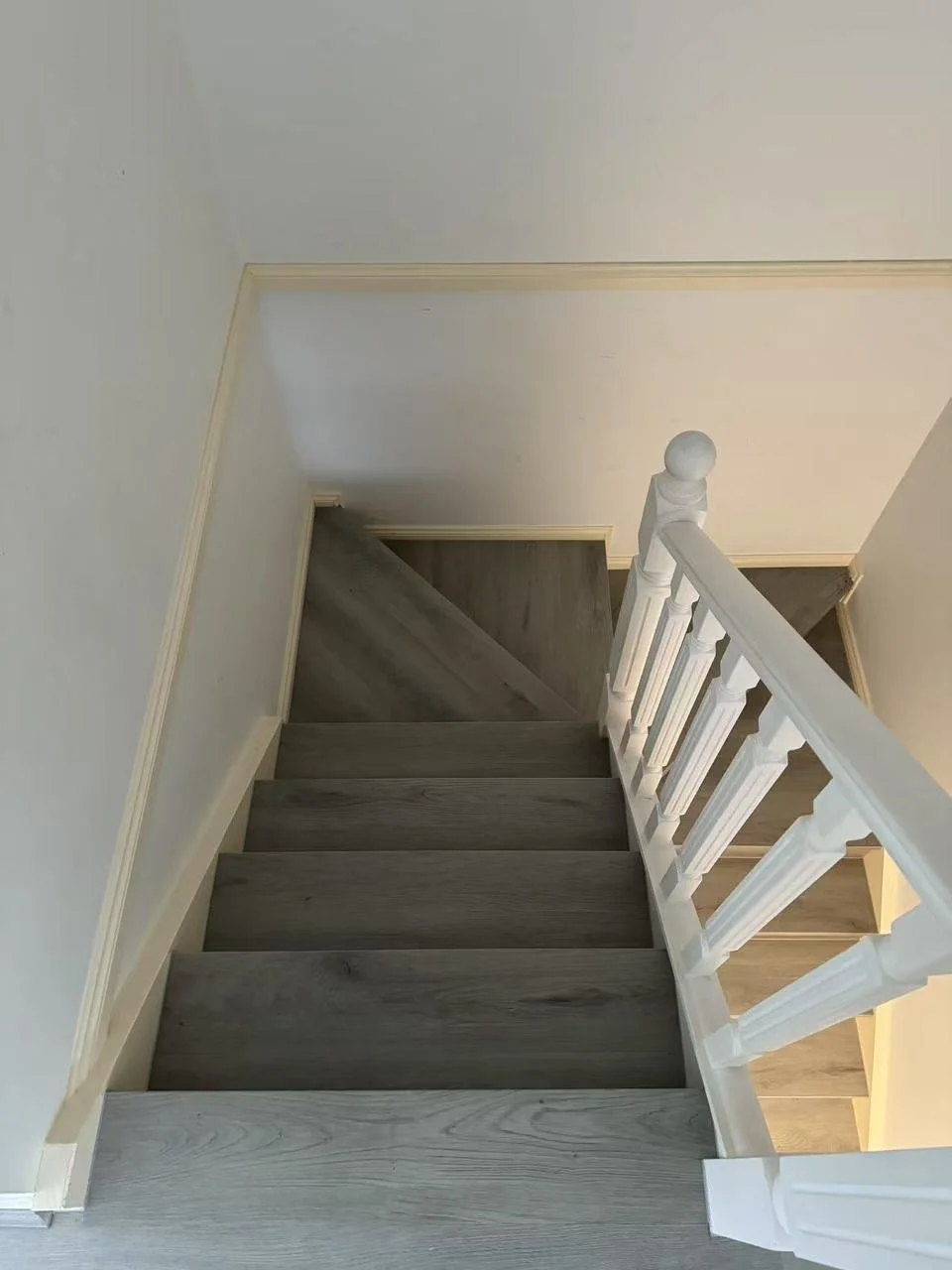 View from the top of a staircase looking down, showing grey wooden steps, white spindled railing, and beige trim on the walls.