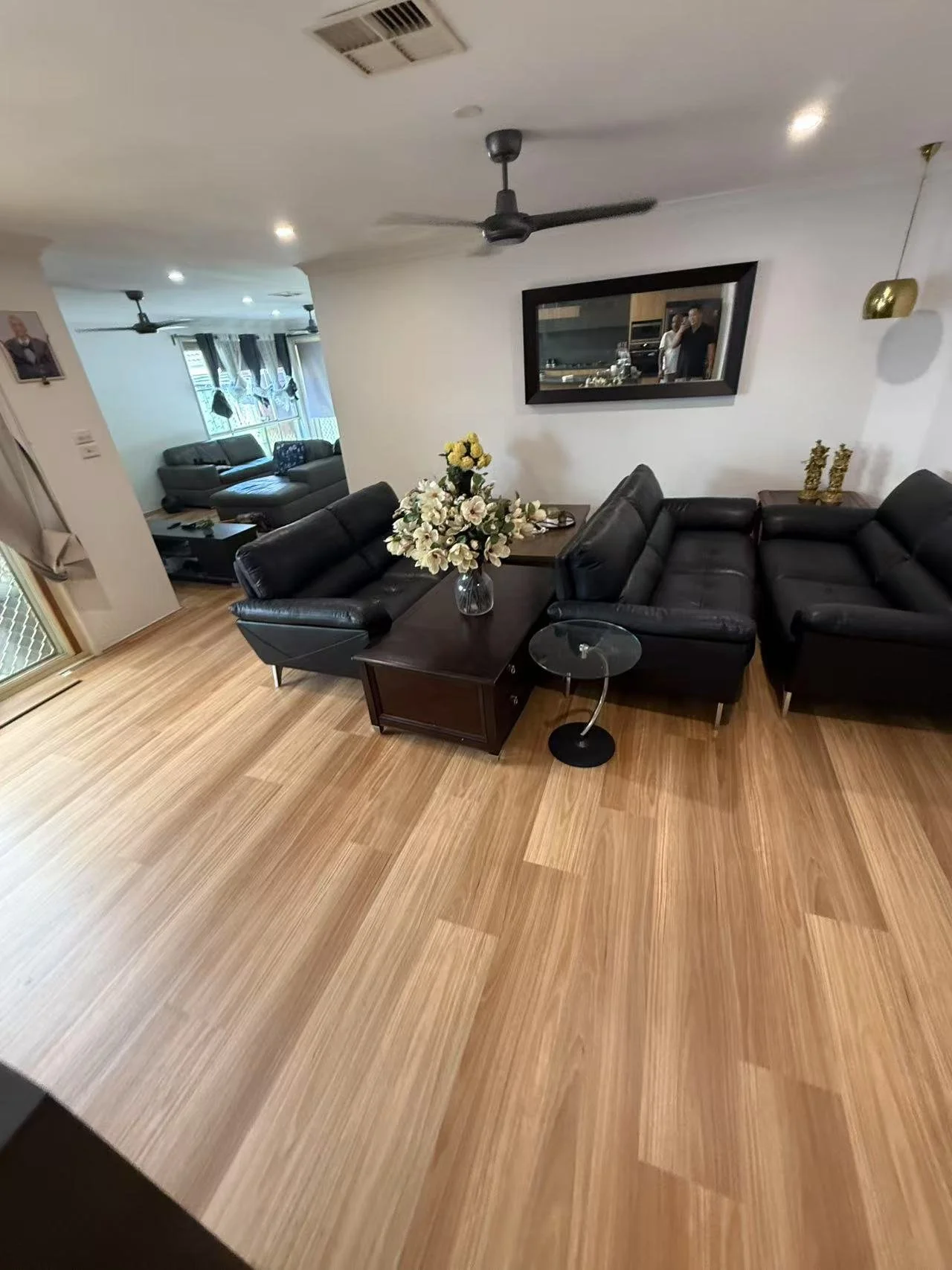 Living room with black leather sofas, a wooden coffee table with a flower vase, and a mirror on the white wall.