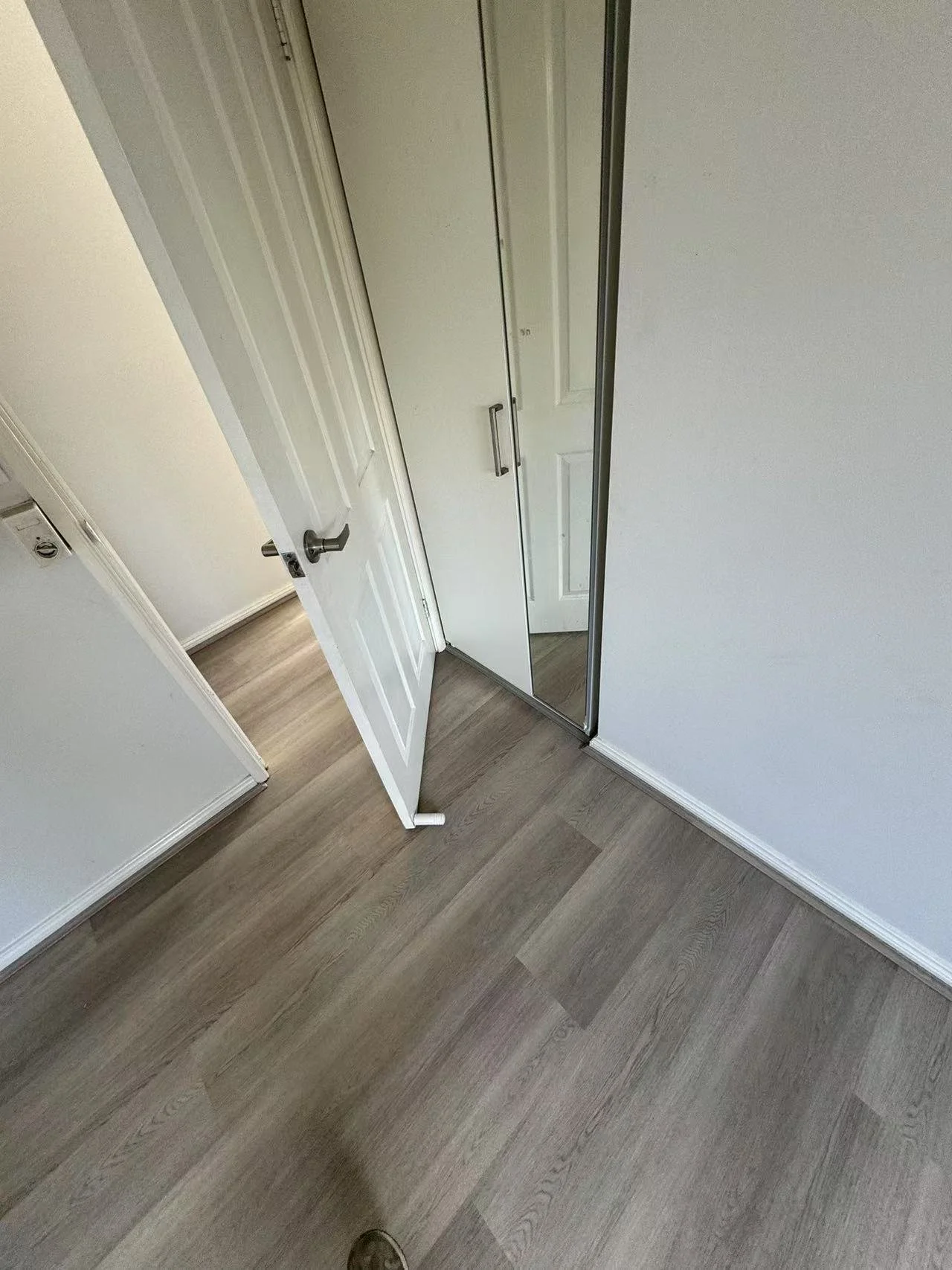 An interior room with wood-look flooring, a closed closet door with a mirror, and a partially open white door.