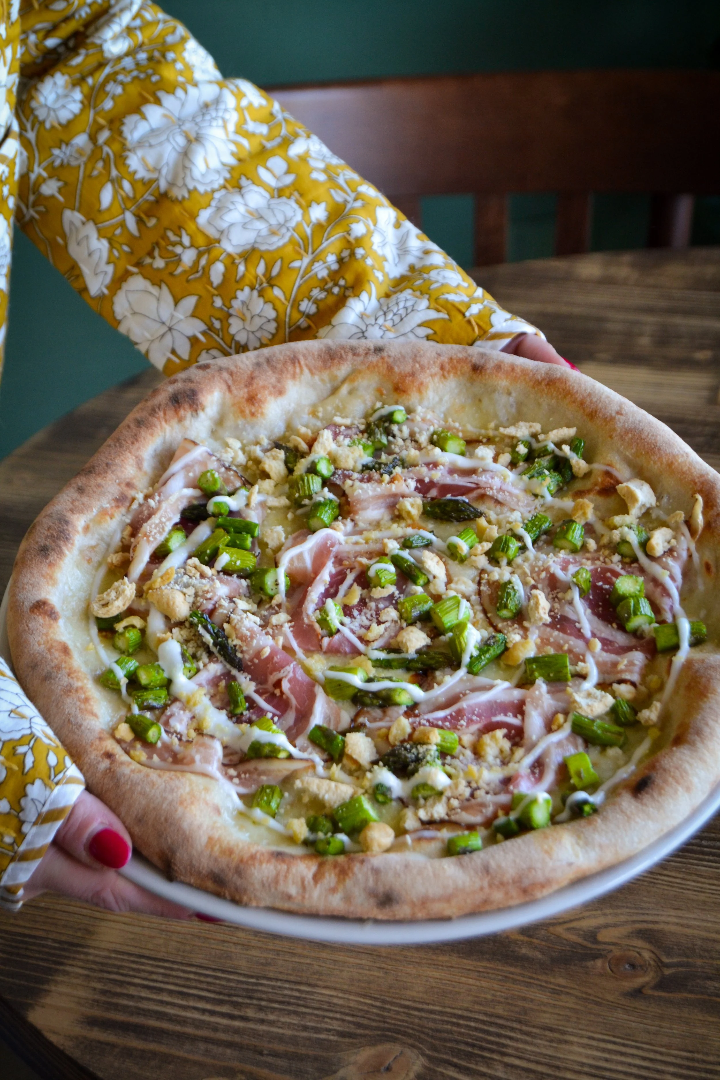 Pizza con prosciutto, fagiolini, e topping di formaggio e salse, su un tavolo di legno.