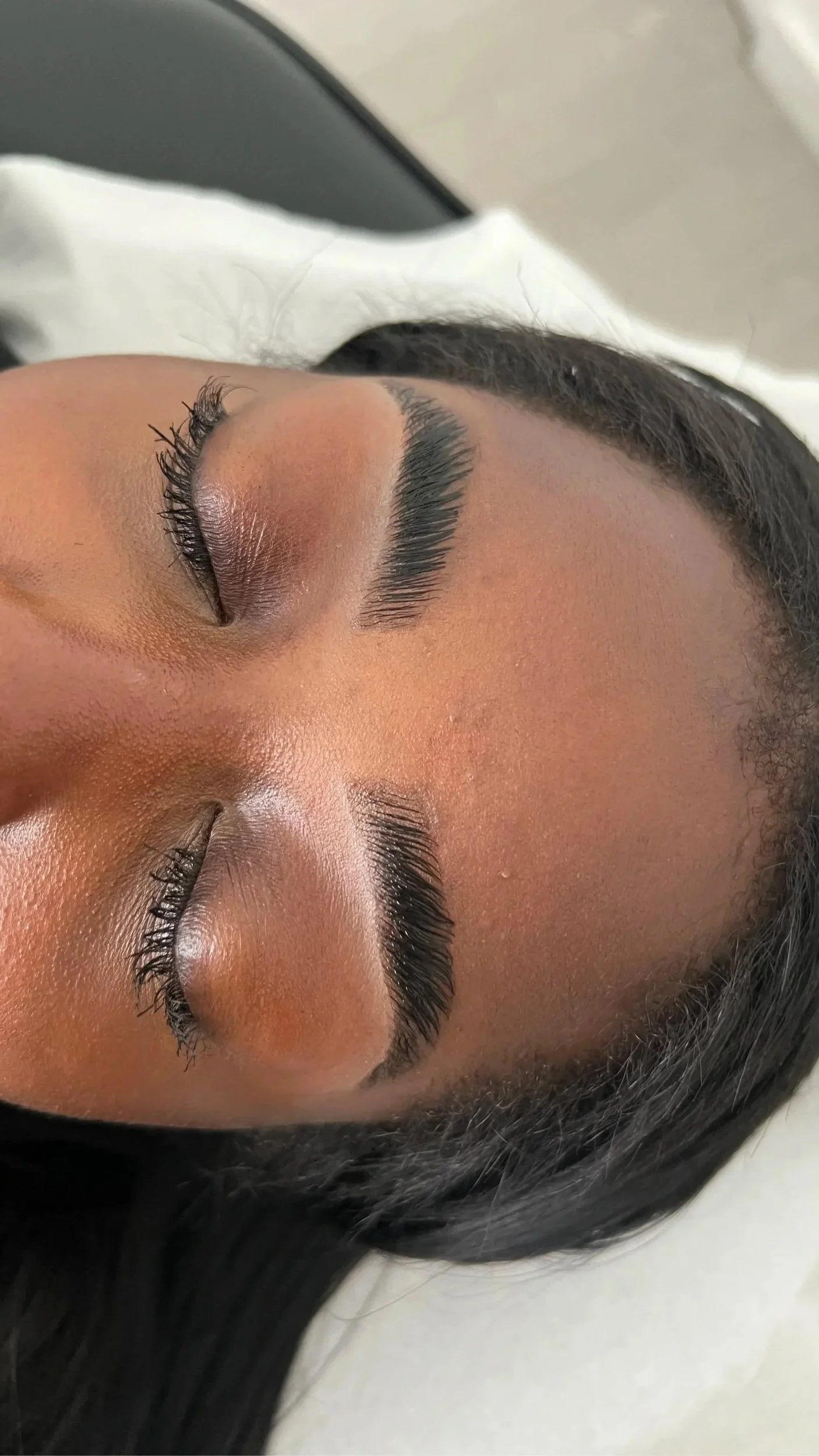 Close-up of a woman's face with her eyes closed, showcasing freshly done eyelash extensions and well-groomed eyebrows.