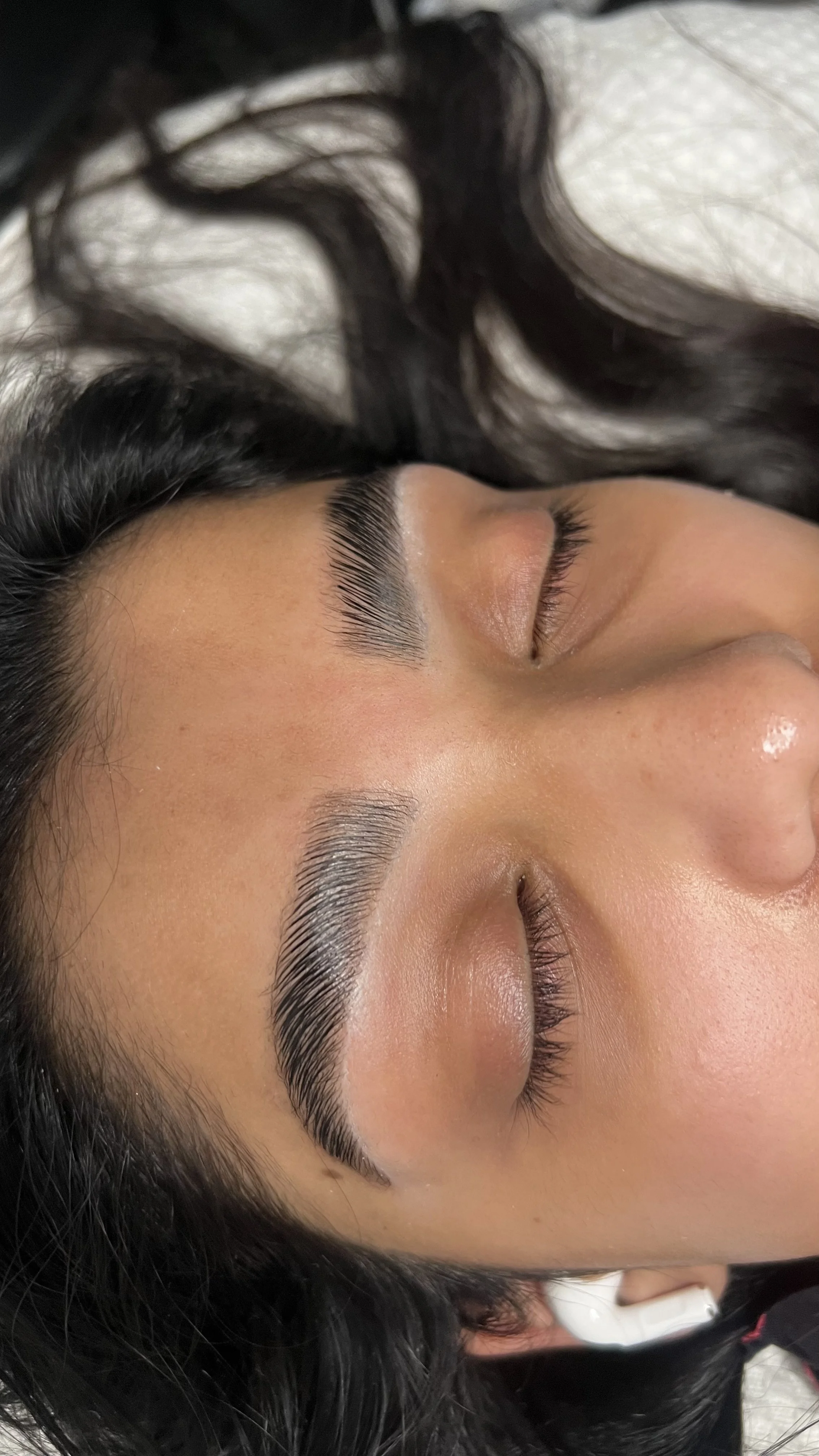 Close-up of a woman's face with well-groomed eyebrows, her eyes closed, and dark hair surrounding her face.