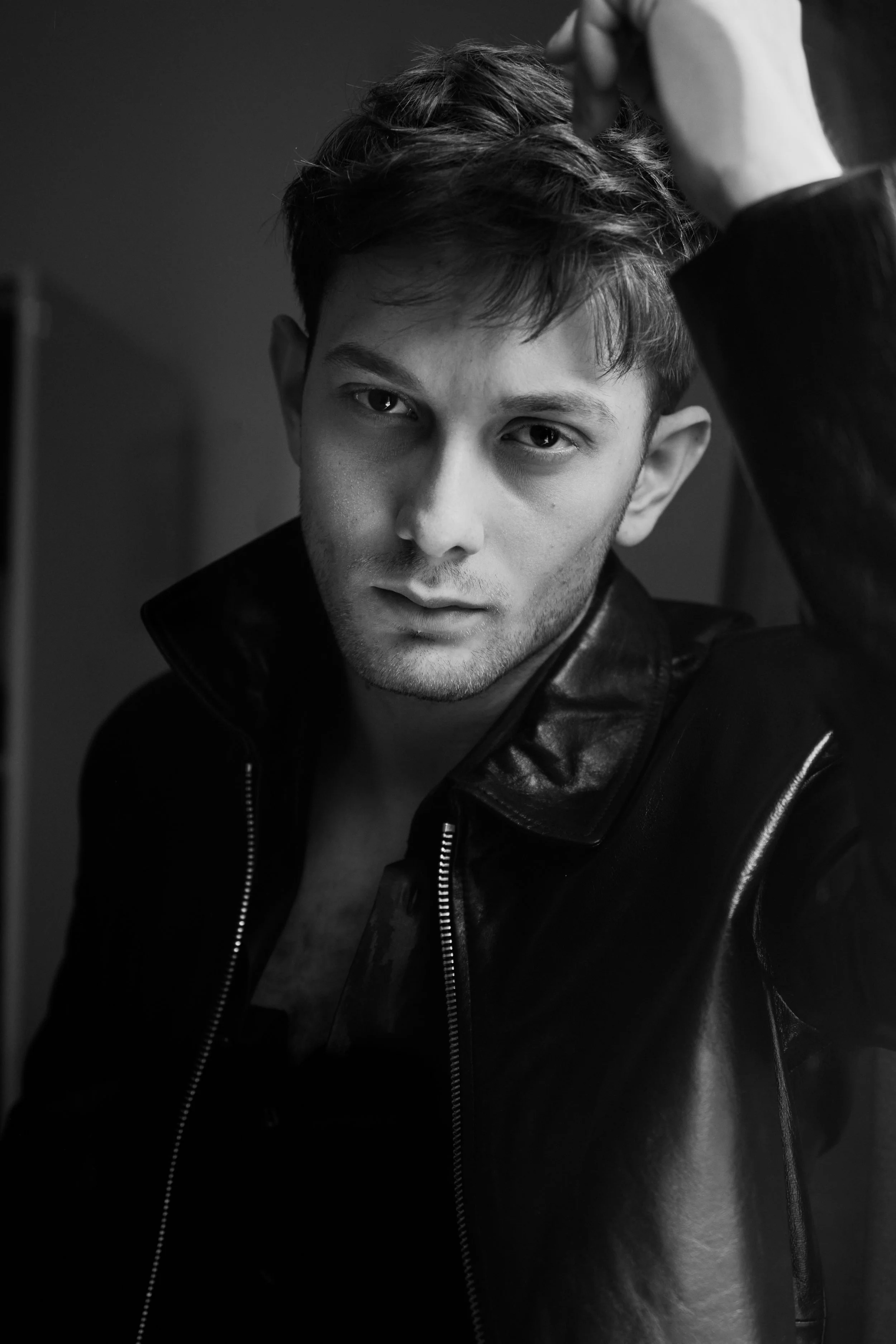 Schwarz-weiß-Fotografie eines jungen Mannes mit dunklen Haaren, der eine Lederjacke trägt.