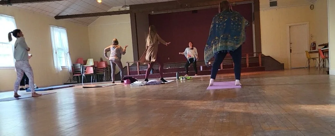 Group somatic stretch in a large room with wooden floors and ceiling beams, participants stretching on mats