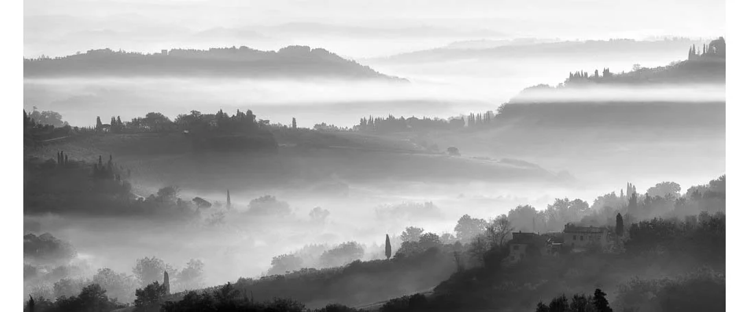 Black and white photograph of the Tuscan hills with morning fog in Tuscany, Italy by Bret Culp, featured in the testimonials section on the homepage.