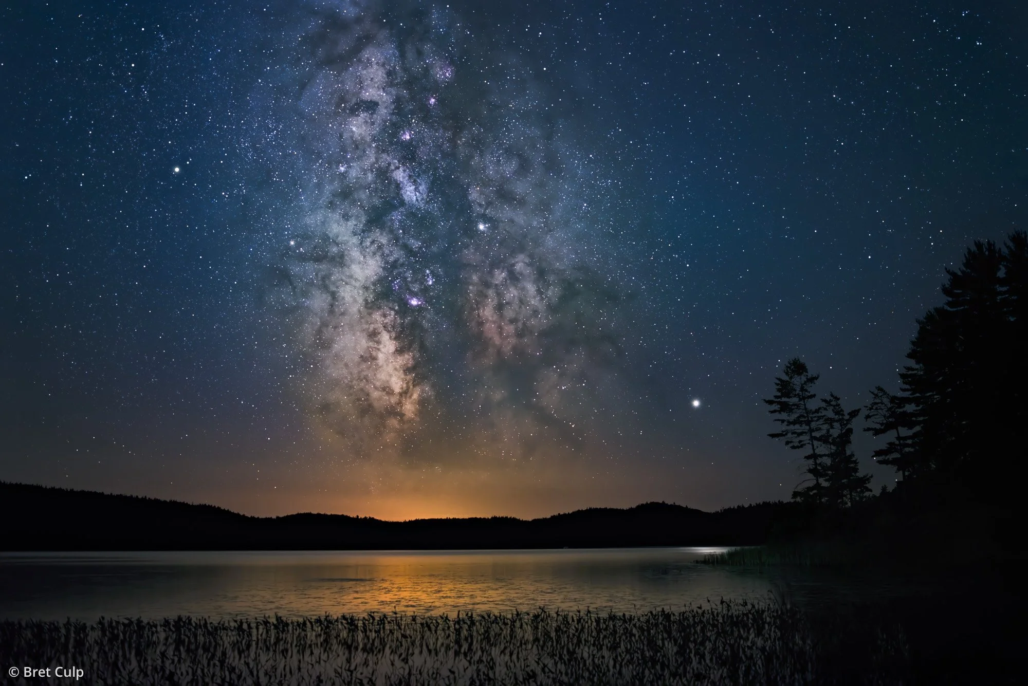 Starry night sky over Algonquin Park, Canada, on July 31, 2019, showing the Milky Way with Jupiter and Saturn, reflected in Grand Lake, by Bret Culp.