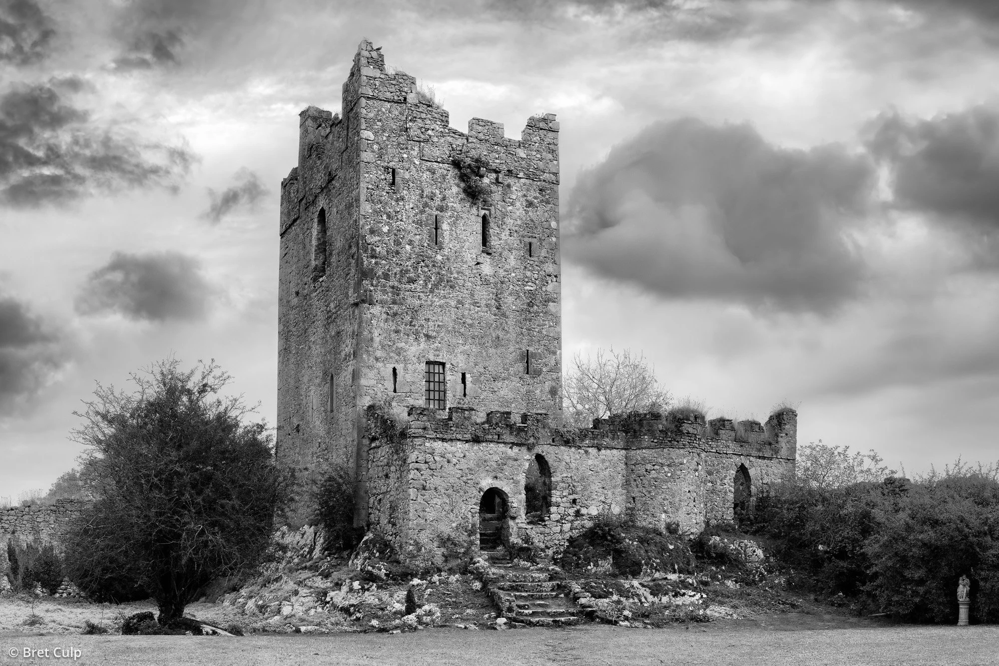 Black and white photo of Clonony Castle ruins in Offaly, Ireland, with dramatic sky and rugged foreground