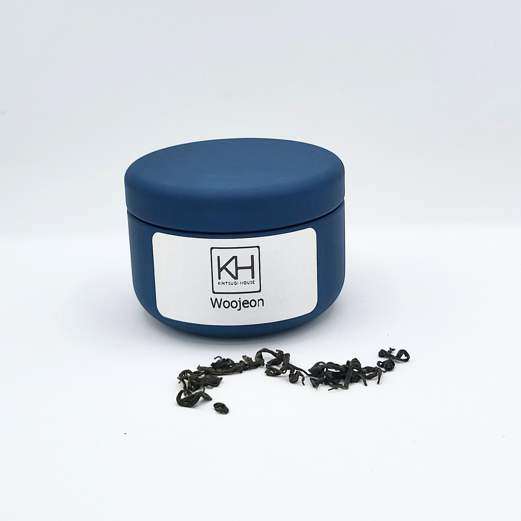Blue tea tin with loose leaf Woojeon tea leaves fanned out on display in front.