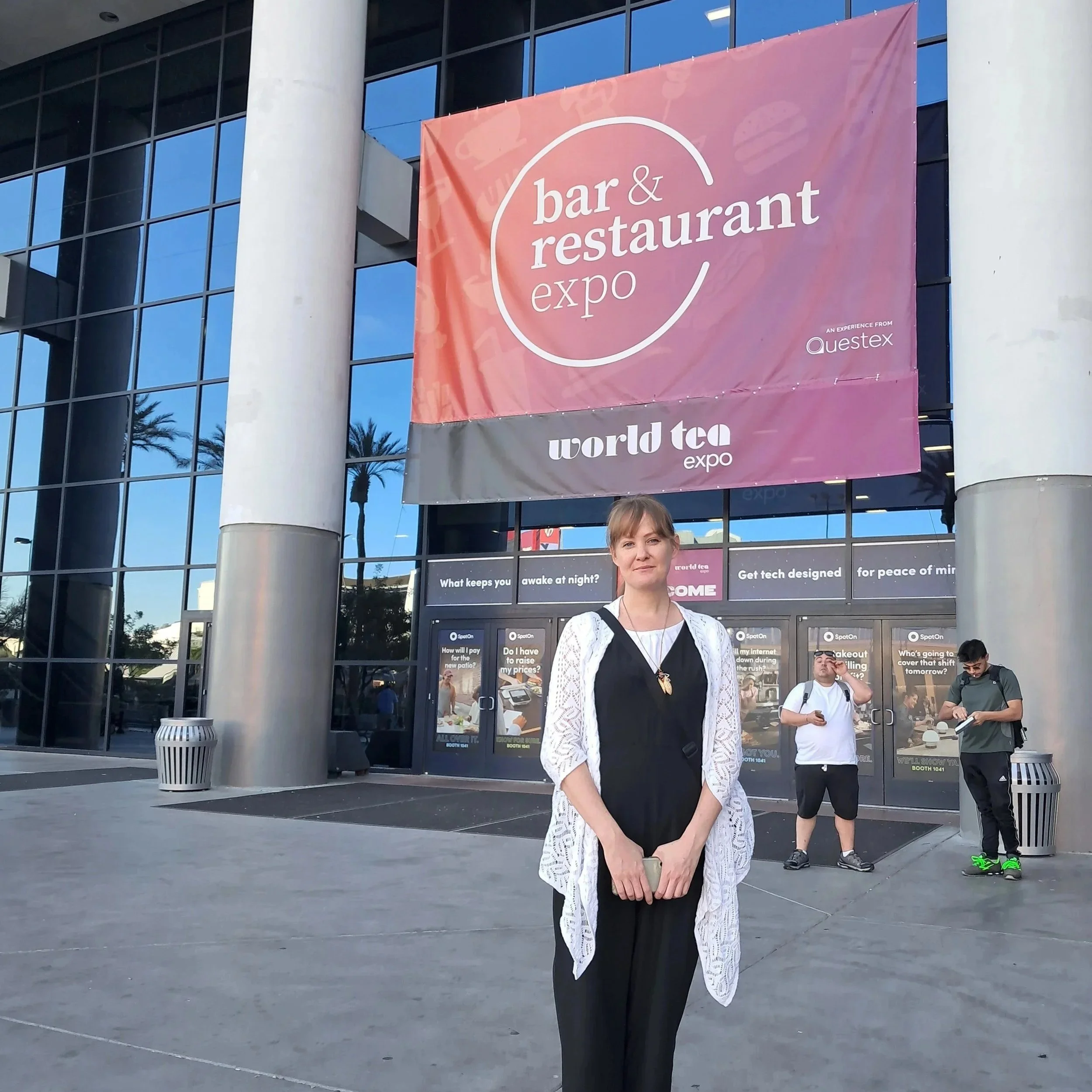 Kintsugi House owner, Andrea Connolly, standing in front of the doors to the Las Vegas Convention Center with a large banner proclaiming World Tea Expo and Bar & Restaurant Expo overhead.