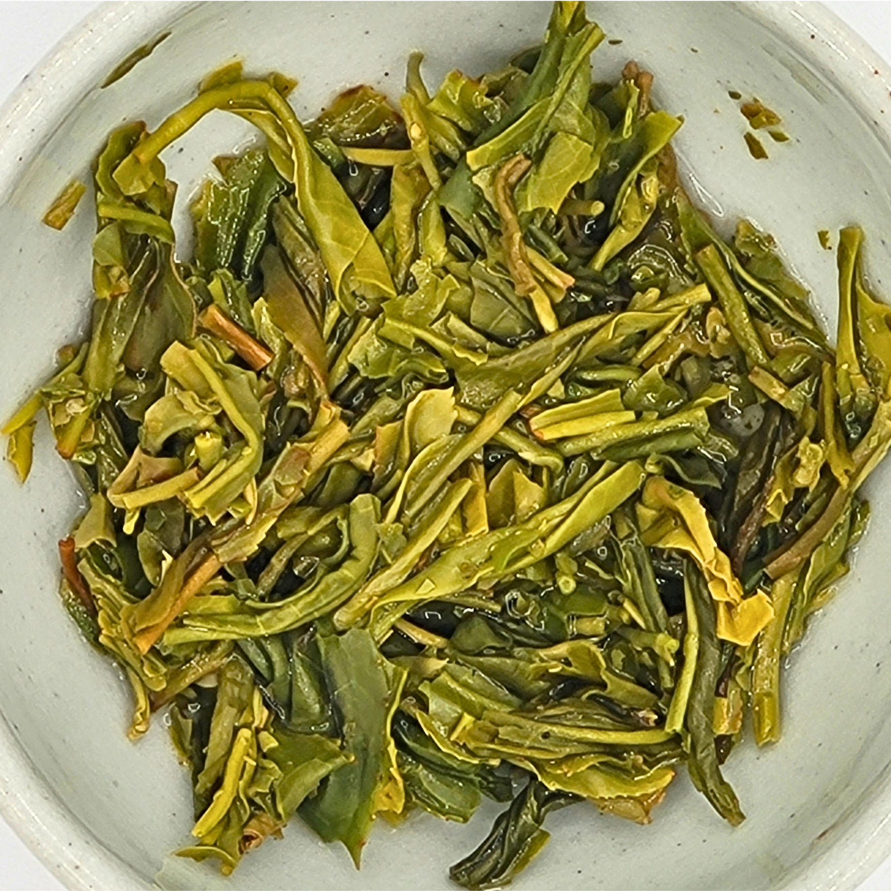 Brewed leaves of Sejak tea displayed in a light-colored glazed cup.