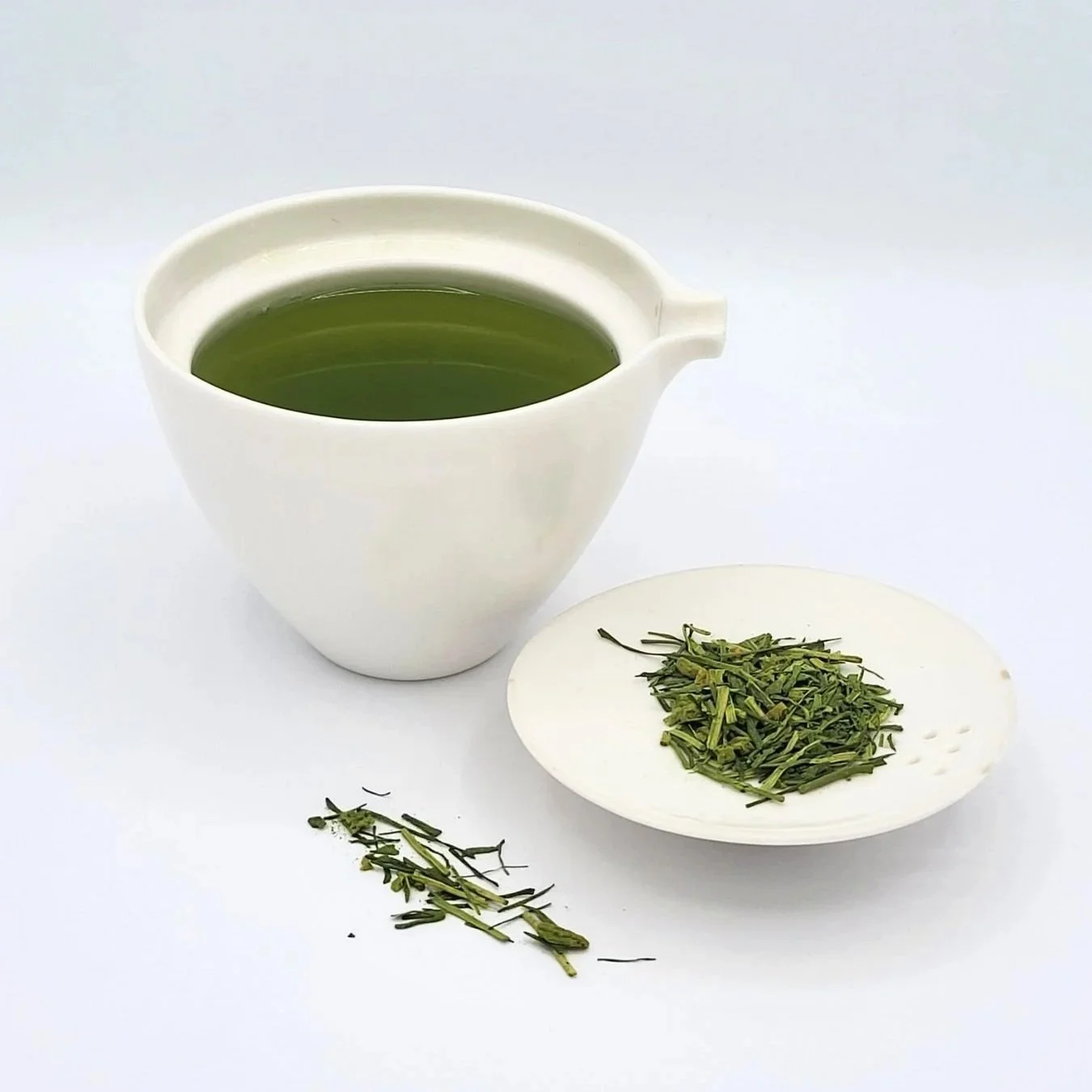 Deep green yuzu kukicha with matcha in a white gaiwan with dry loose leaf displayed in the white gaiwan lid.