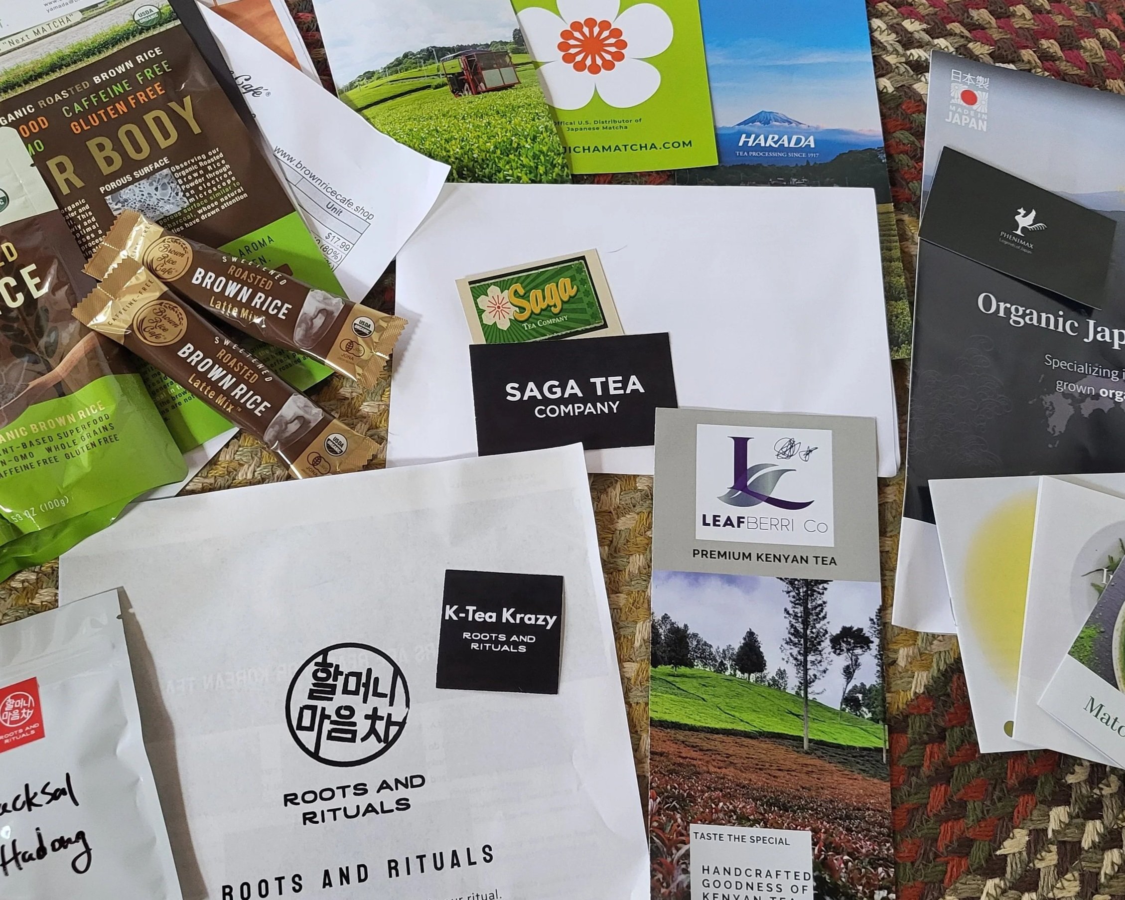 An assortment of flyers and samples from tea wholesale companies arranged on a woven background.