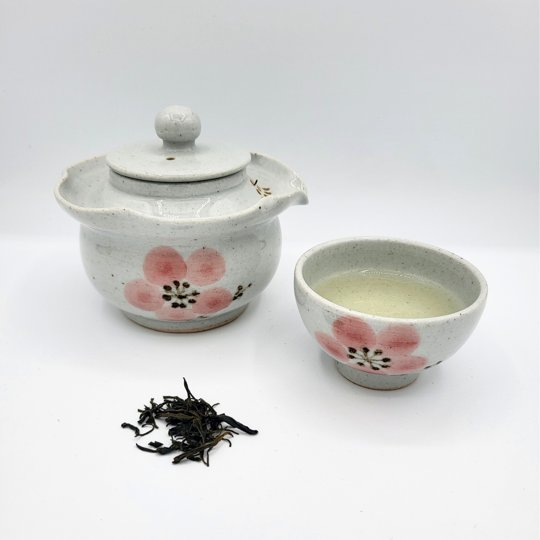 Small Korean-style gaiwan and cup with pink cherry blossom filled with brewed Sejak tea and a small mound of loose leaf Sejak displayed in front.