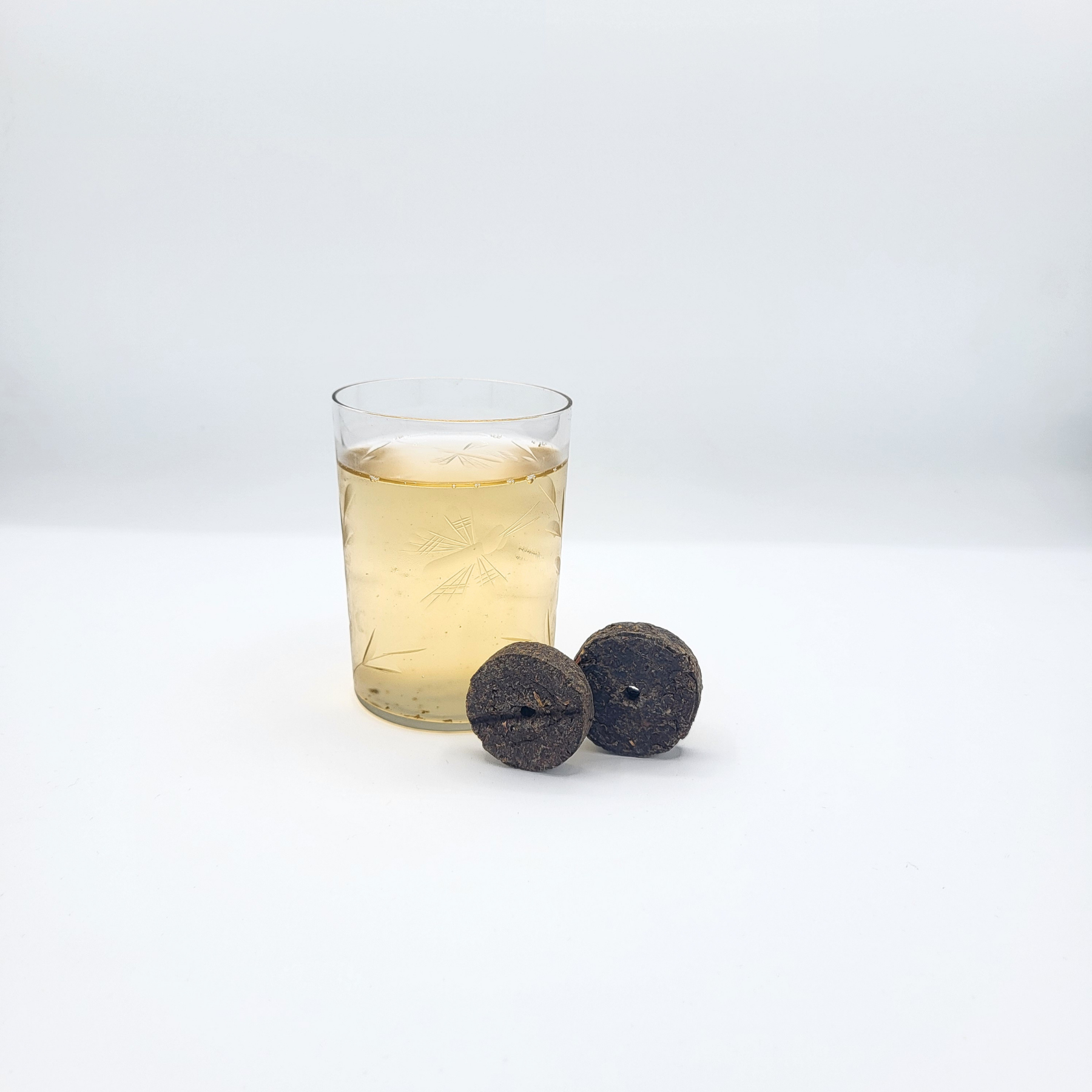 Crystal glass of golden colored brewed doncha beside two discs of coin-shaped doncha tea.