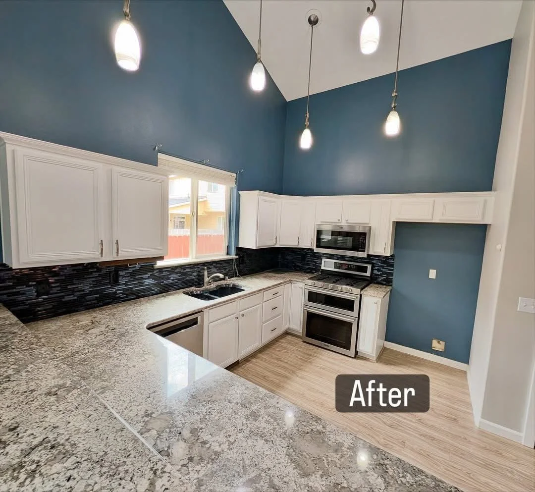 Modern kitchen with white cabinets, granite countertops, dark backsplash, stainless steel appliances, blue walls, and pendant lighting.