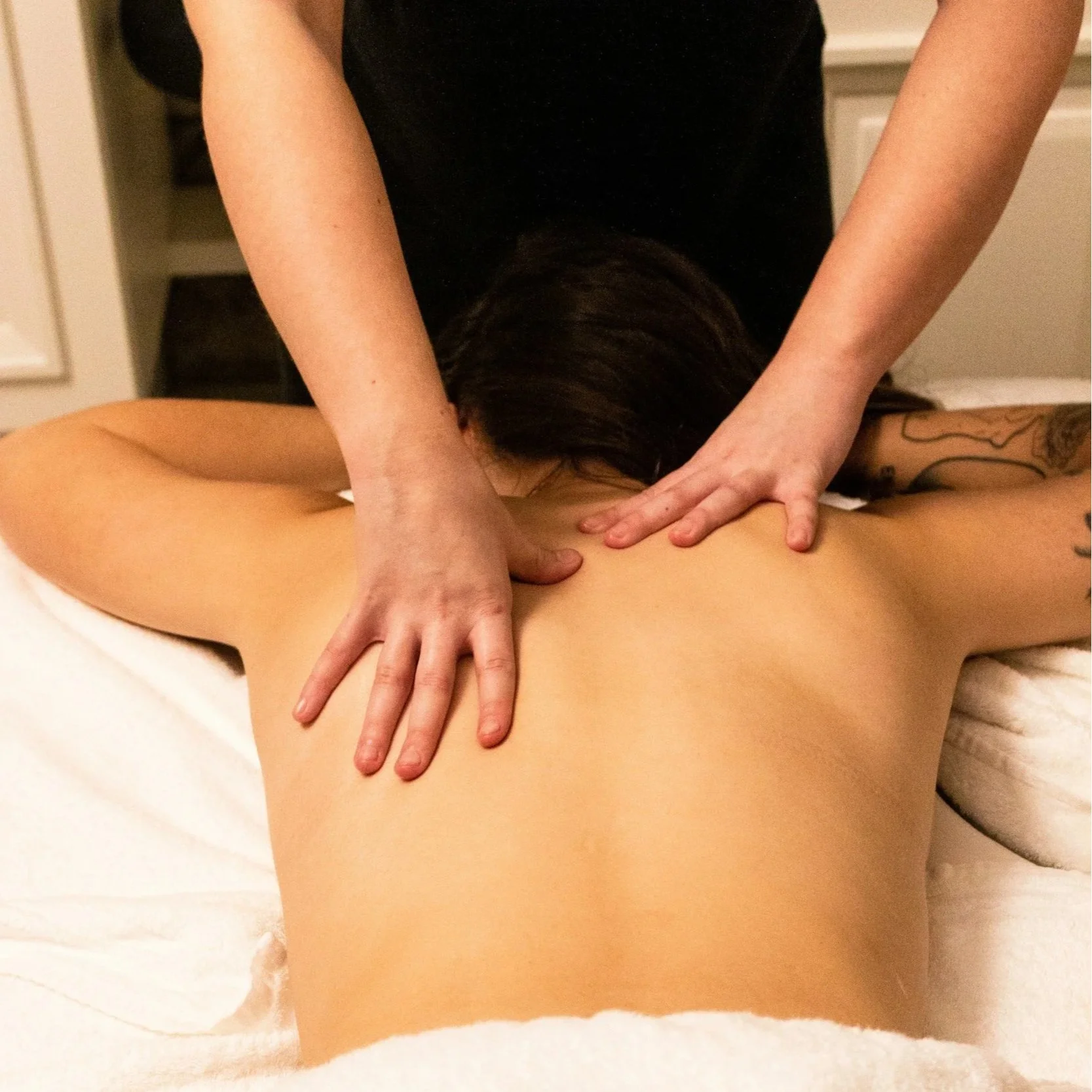 A person receiving a massage on their back from a massage therapist in a spa room.