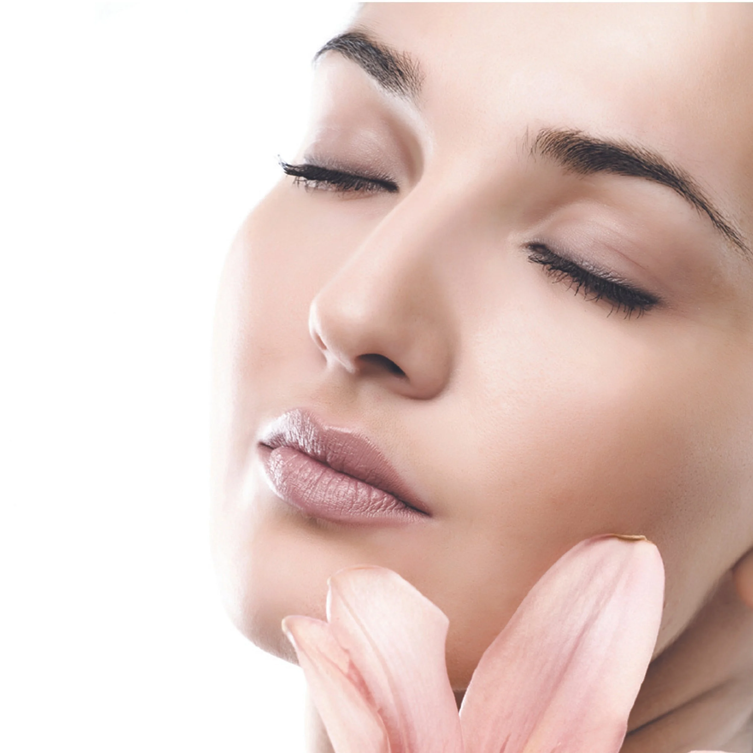 Close-up of a woman's face with closed eyes, smooth skin, and pink lips, holding a pink flower near her chin.