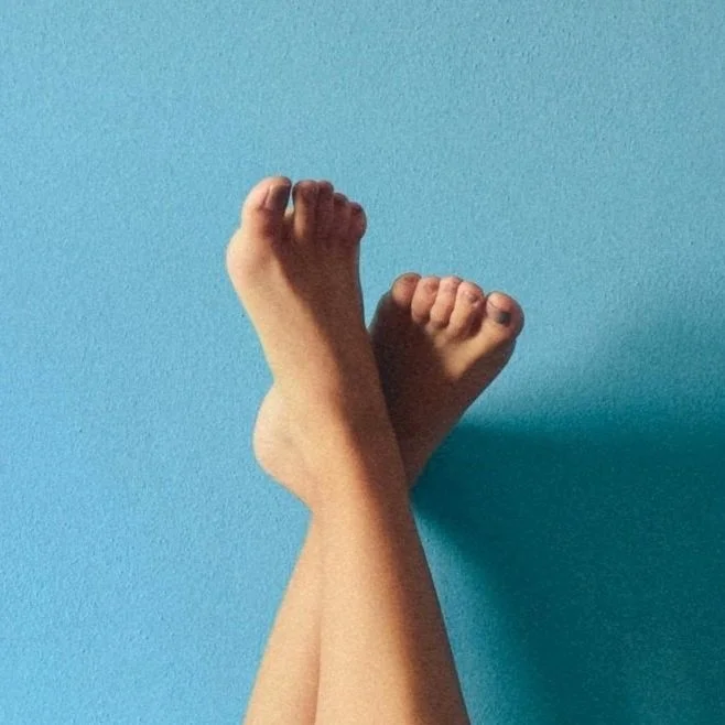 Two bare feet crossed at the ankles against a blue wall.