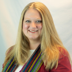 A woman with long blonde hair smiling against a light background, wearing a colorful striped scarf and a red top.